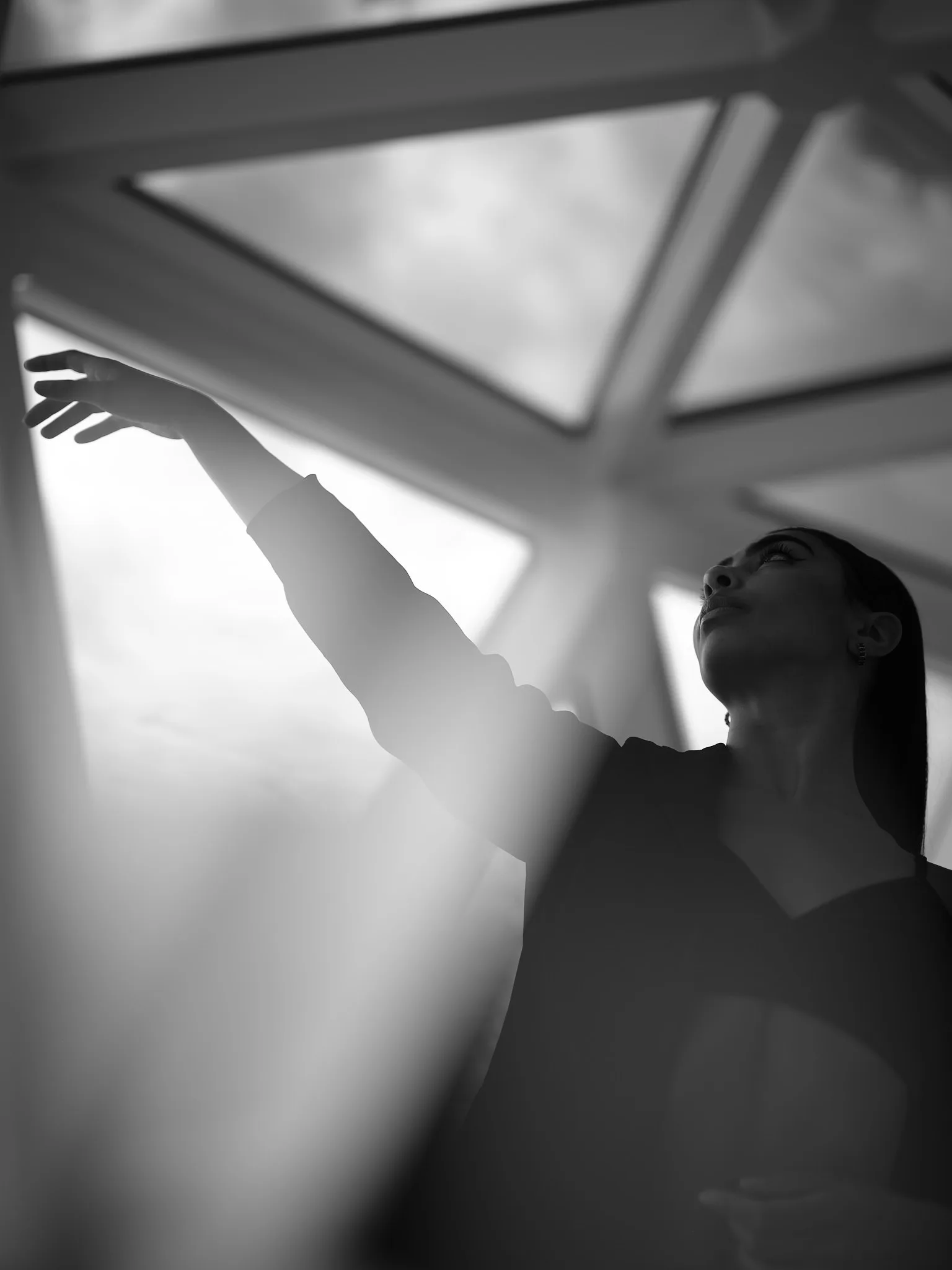 woman reaching toward glass ceiling beams — portrait photography by Tom Kubik