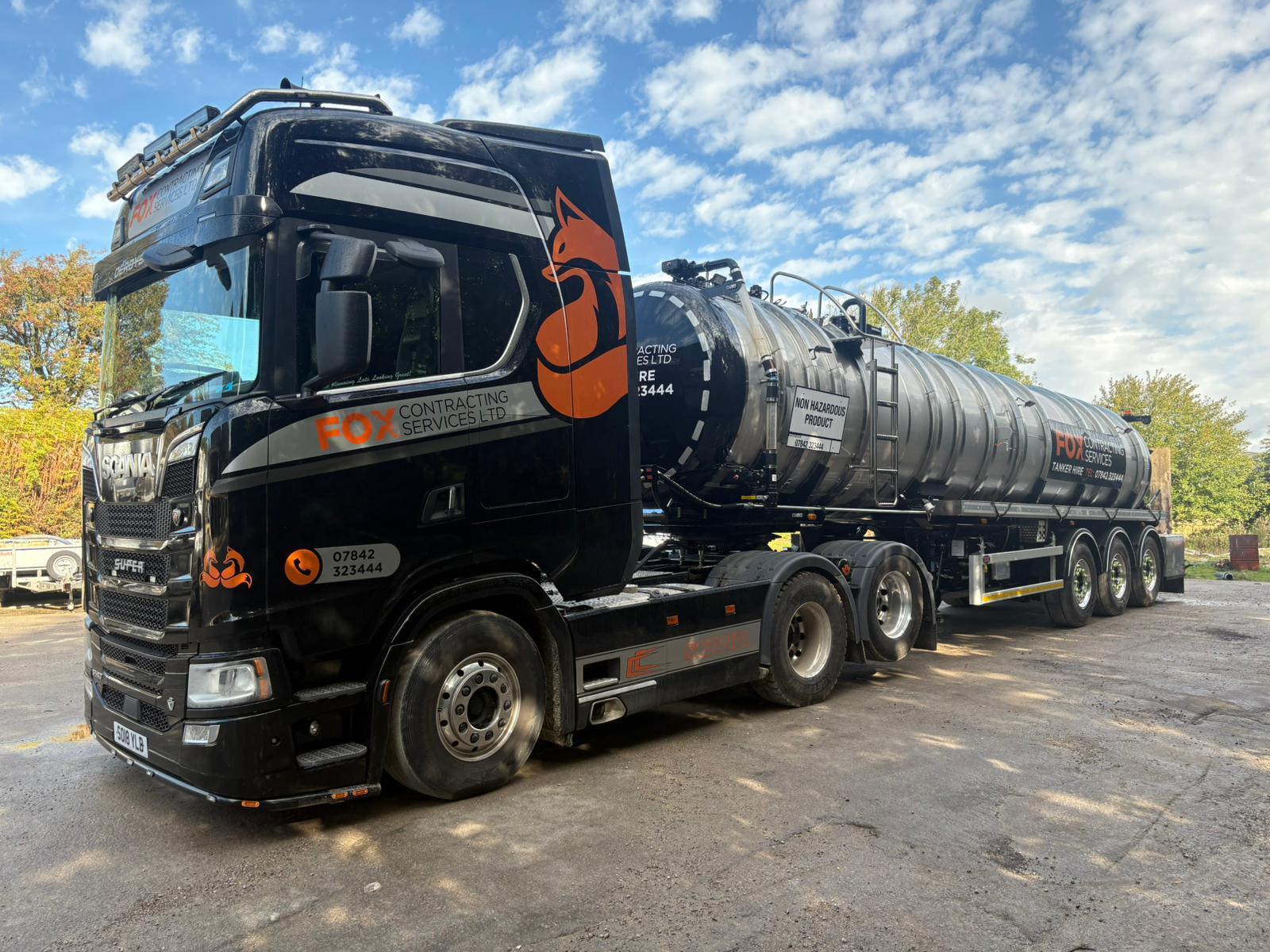 Tanker truck parked outside an industrial plant at night, with the building lit by floodlights.