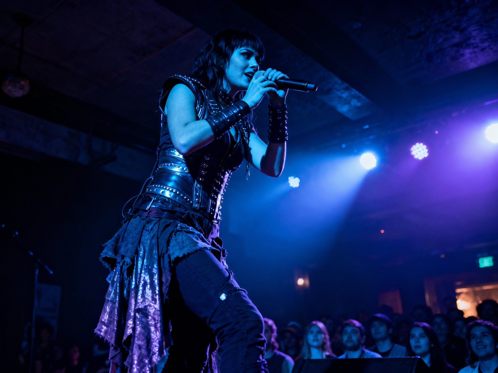 An atmospheric wide landscape image of a female rock singer mid-performance on an intimate indoor