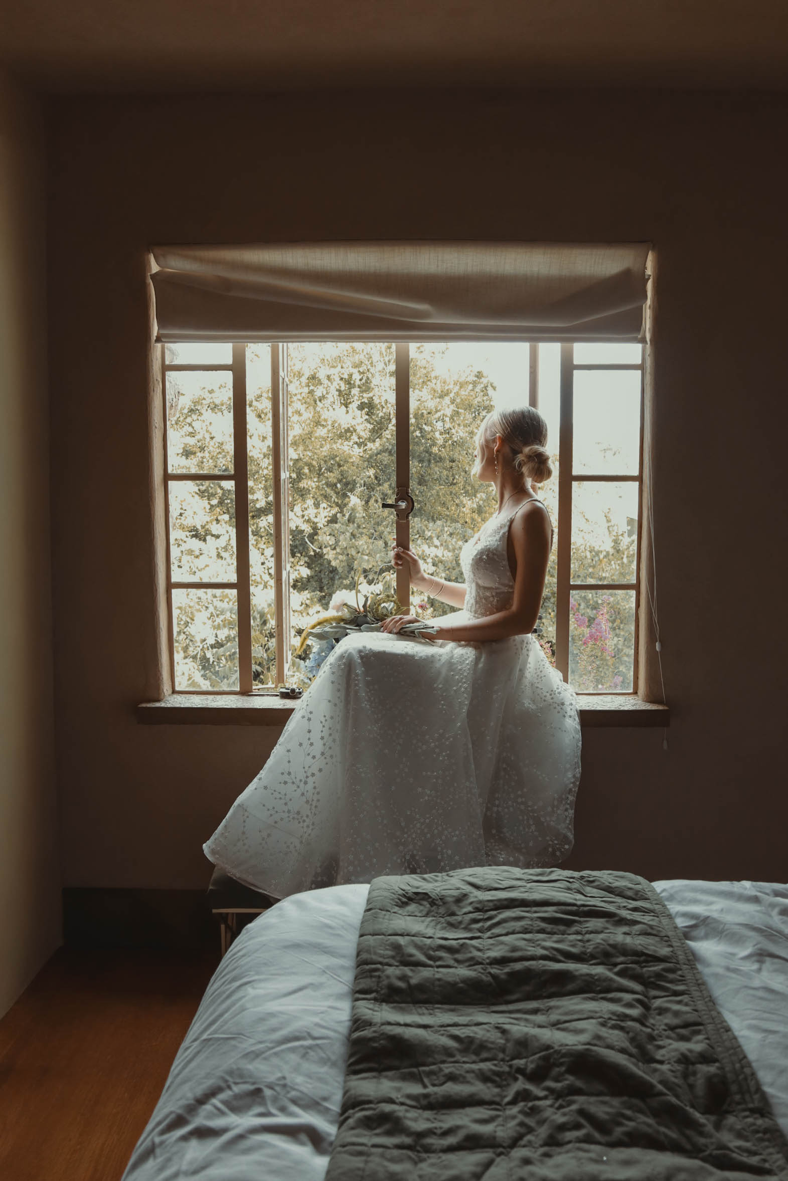 Bride sitting in window sill looking out at her groom. 