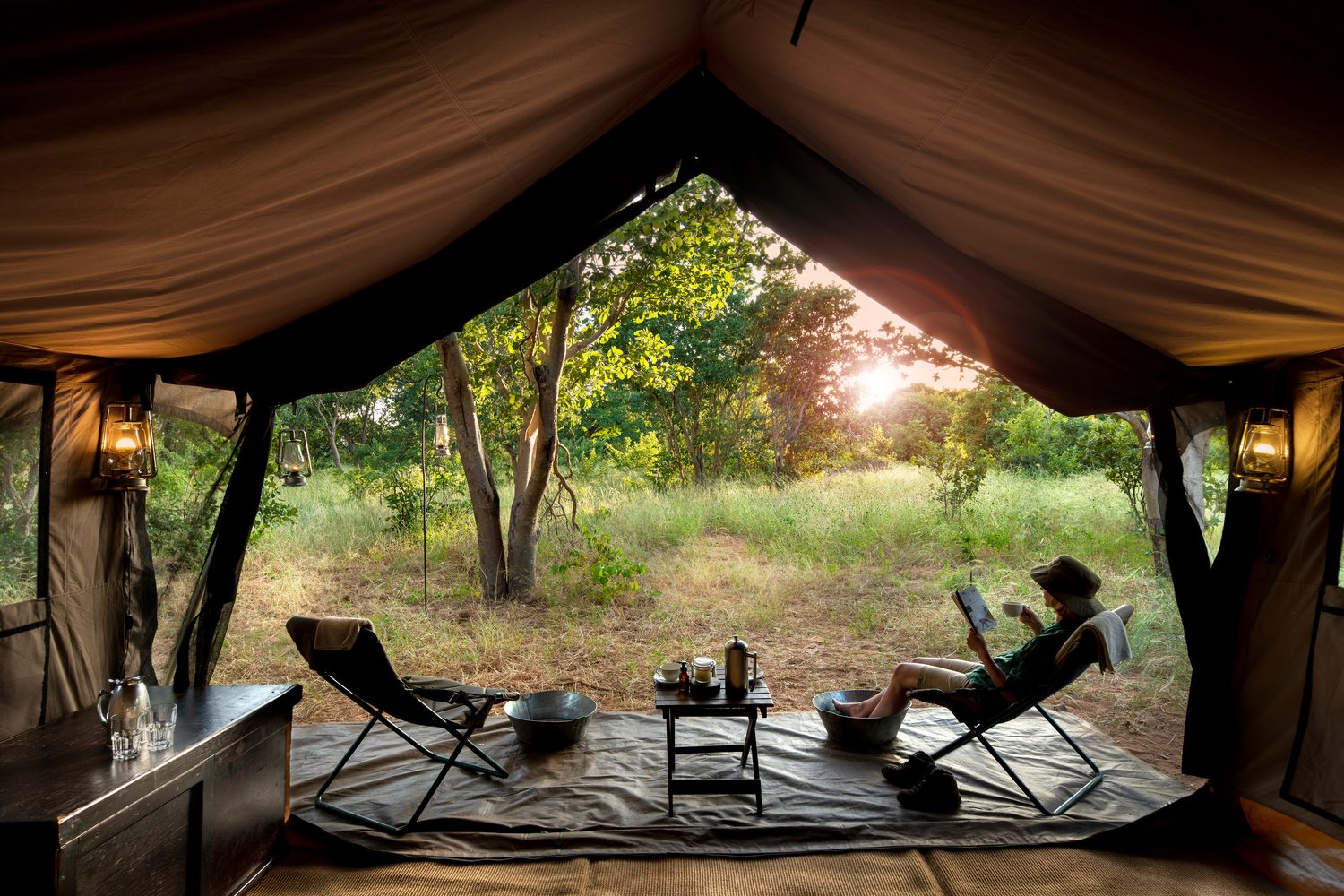 A guest reading in a camp chair at the open flap of a canvas tent