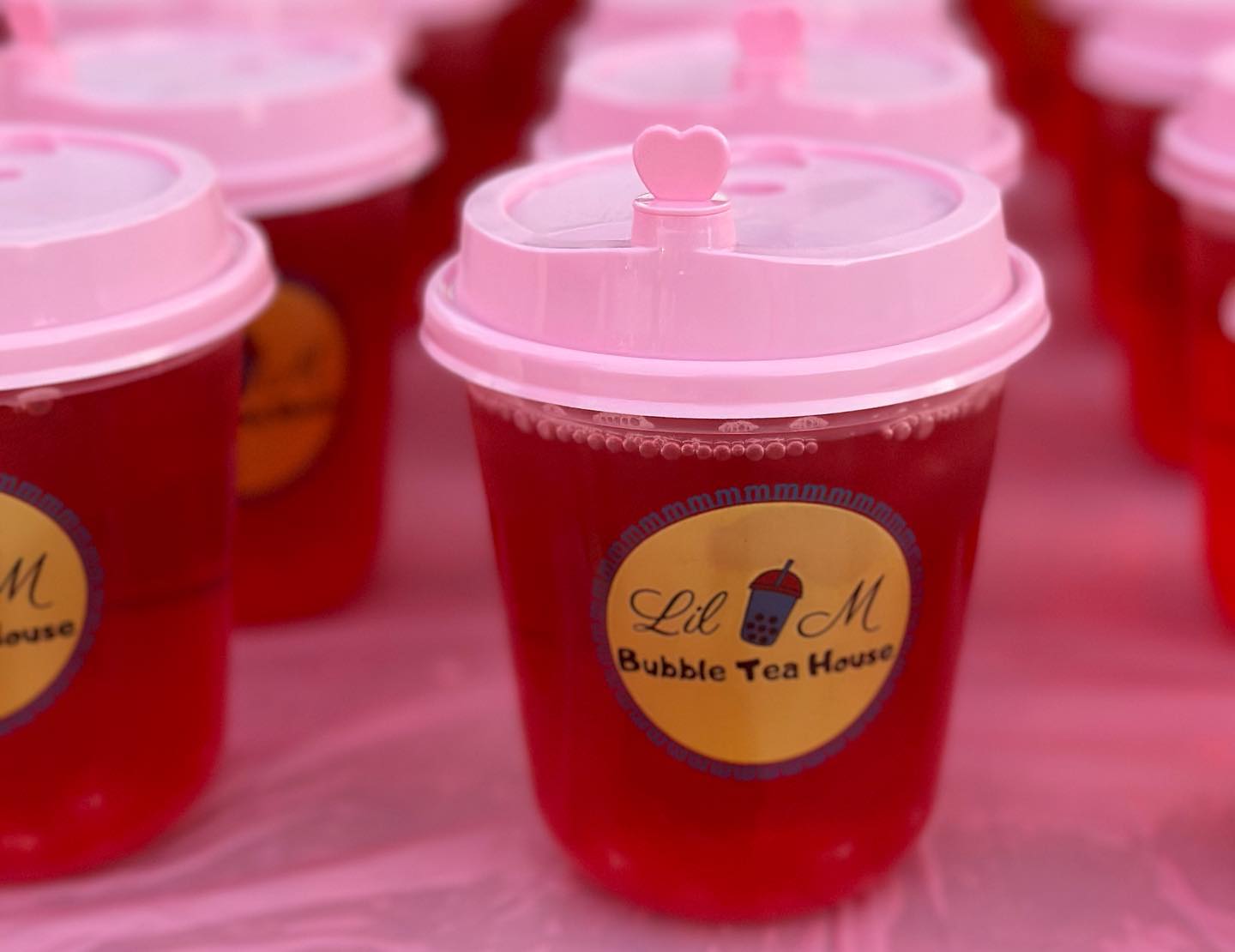 Lil M Bubble Tea’s bright red fruit tea served in an adorable pink cup with a heart-shaped topper, adding a playful touch to this flavorful drink.