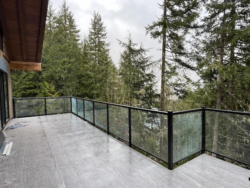 Frameless glass railing installed on an elevated patio of a modern home, overlooking tall evergreens in a forested BC landscape.