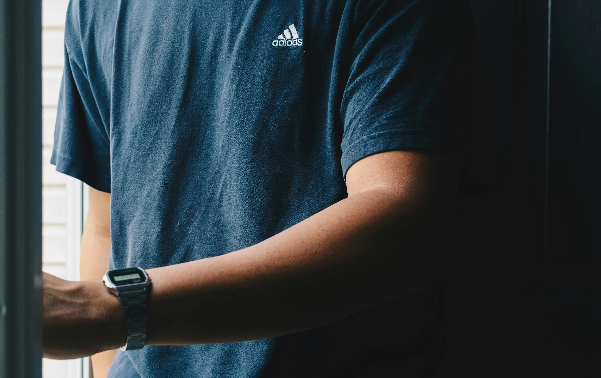 Man wearing casual t-shirt and smartwatch near window, modern lifestyle fashion detail