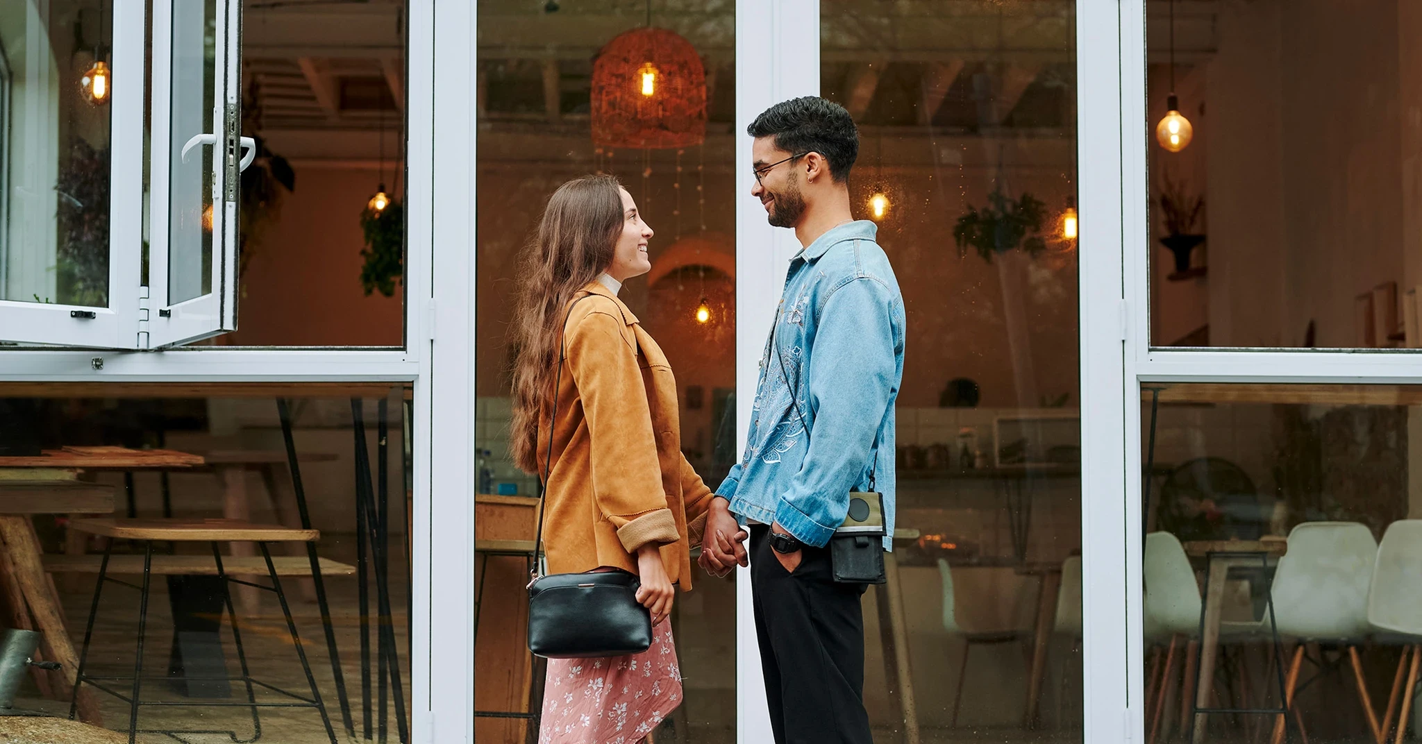 En ung kvinna och en man står och ser kärleksfullt på varandra med en glasfasad i bakgrunden, som leder till ett café.