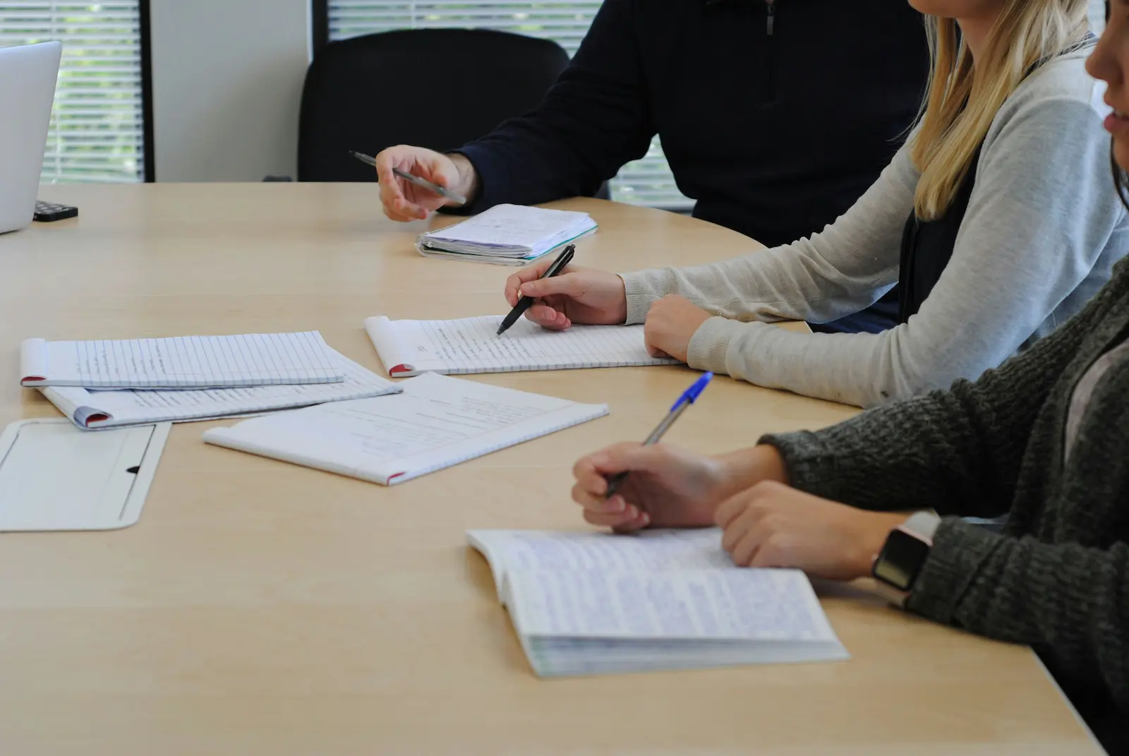 A small group seated at a table writing in notepads, with papers spread out in front of them.