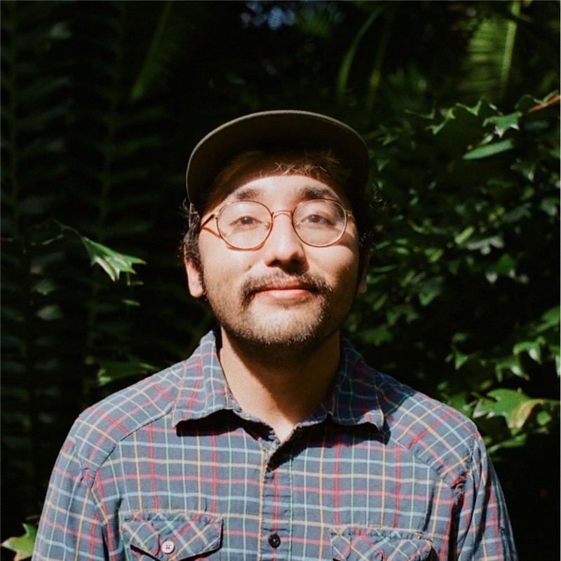 A portrait photo of Enriwue Sampson, a lighter-skinned person wearing a plaid shirt and baseball cap.