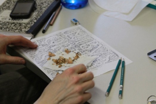 A photo of a piece of paper with sketched typography letters, two green crayons and some pieces of sharp pencil.