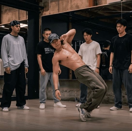 Street dancer performing a dynamic hip-hop move while a group of dancers watches in a studio setting