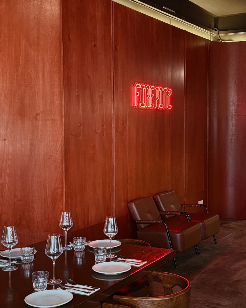 Interior view of Fire Pitz steakhouse featuring a wooden wall, a neon sign that says 'FIREPITZ', and a dining table set for guests.