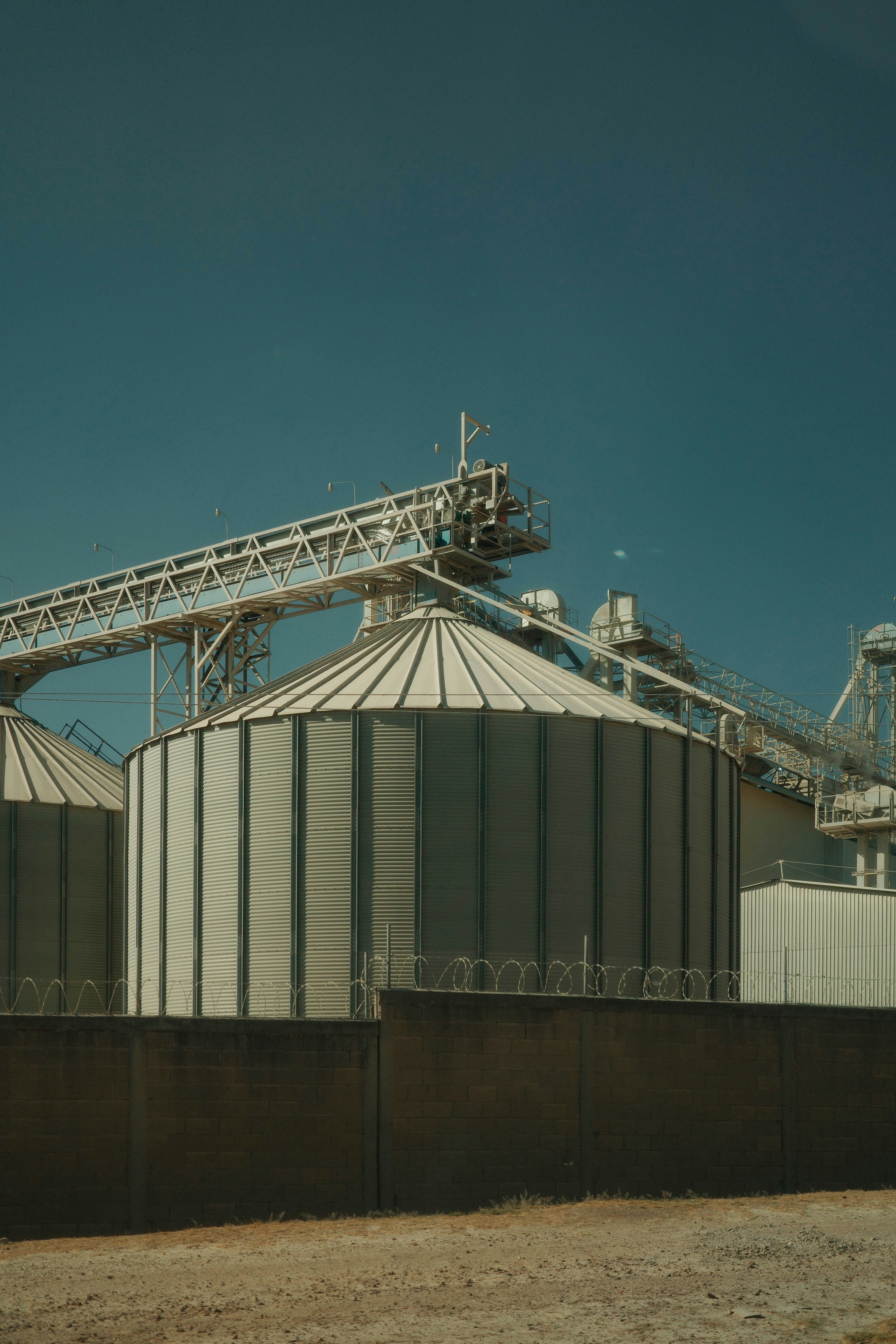 Industrial silos with conveyor belts under a clear sky.