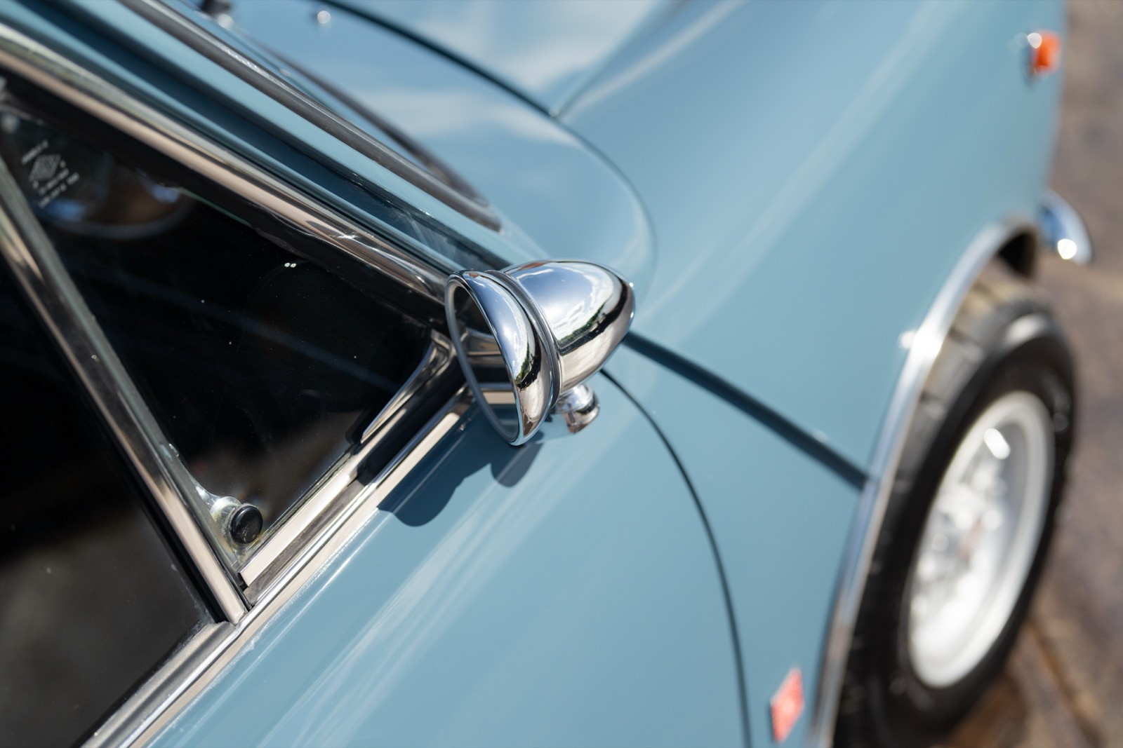 Close-up view of a vintage blue car's side mirror and window, showcasing its classic design and shiny finish.