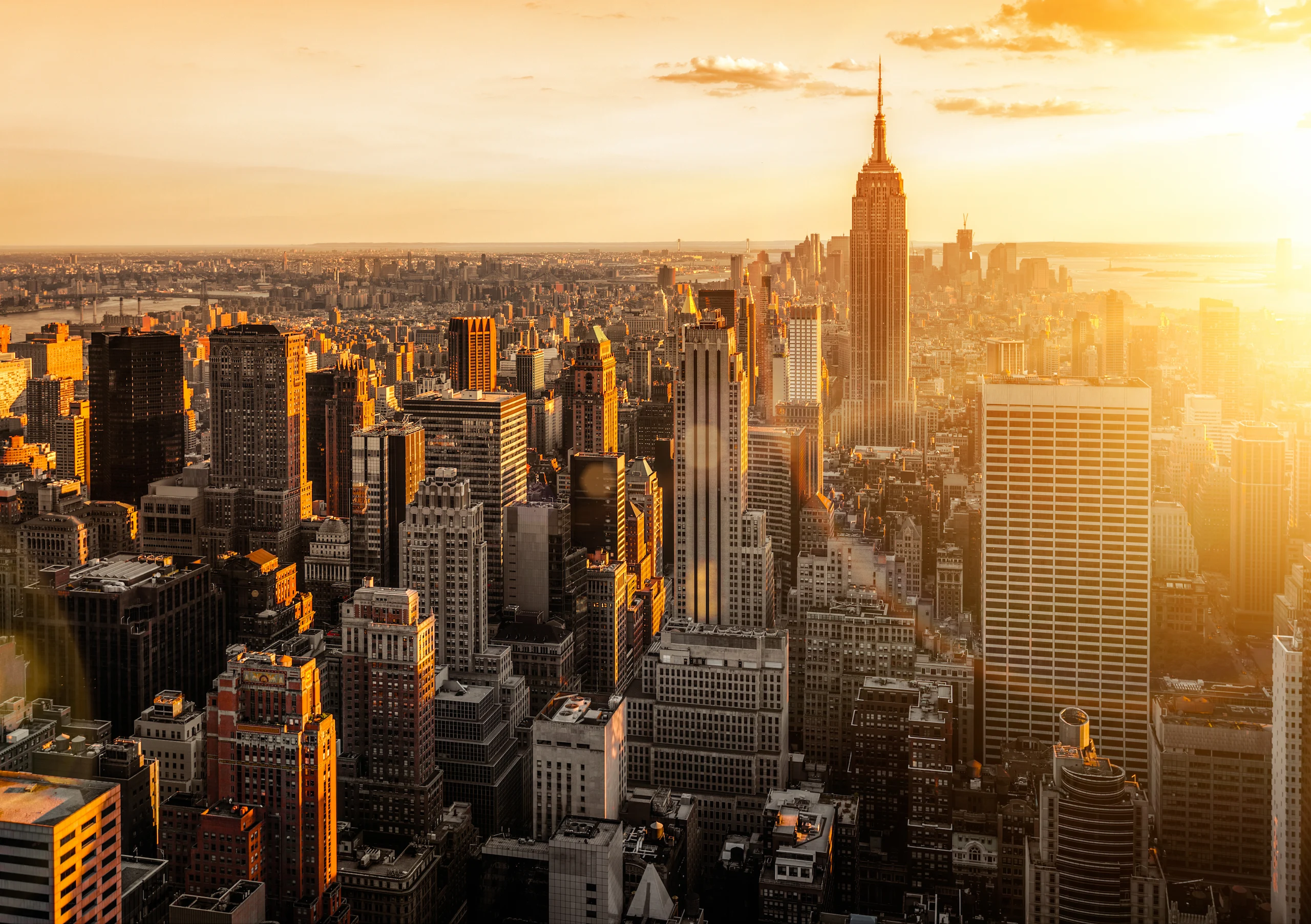 Aerial view of the NYC skyline at sunrise, capturing iconic skyscrapers and the glowing cityscape as the sun rises over Manhattan.