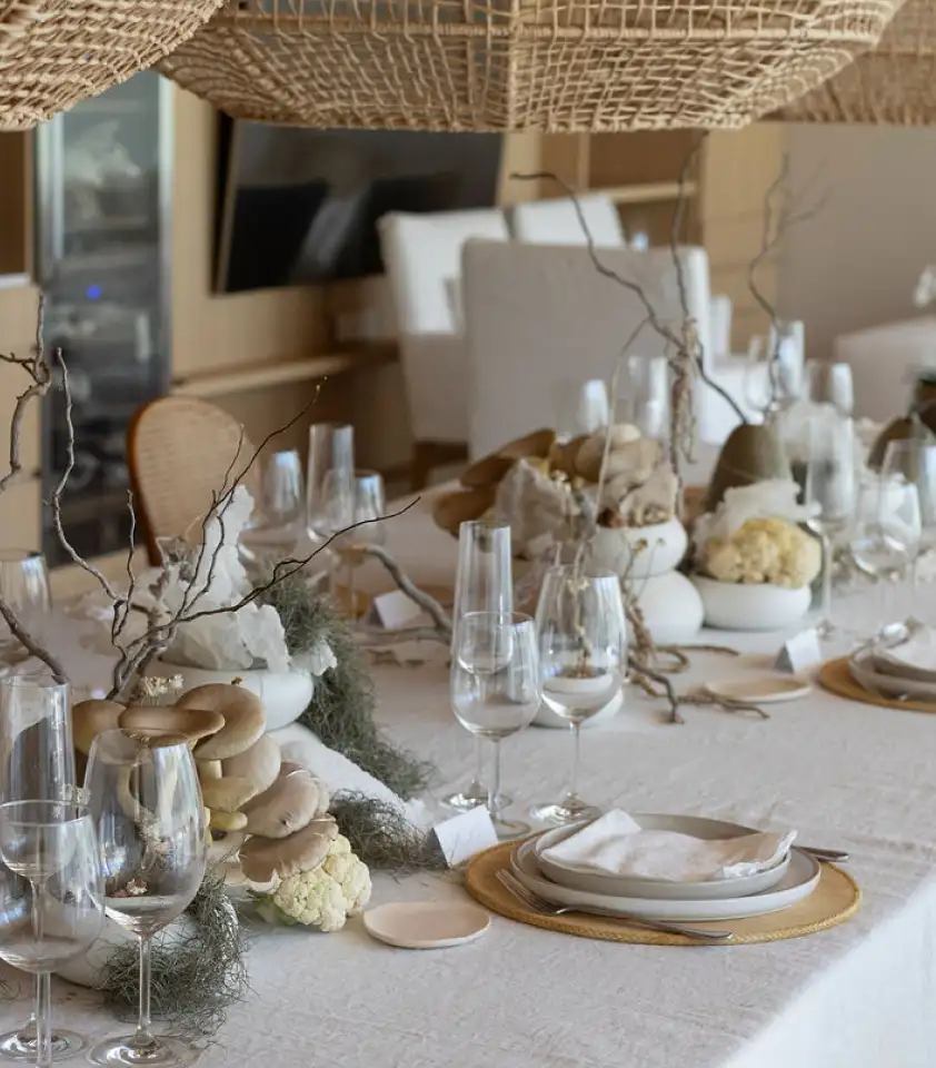 Mesa elegante con decoración en tonos neutros y texturas orgánicas, arreglos florales con hongos y ramas secas.