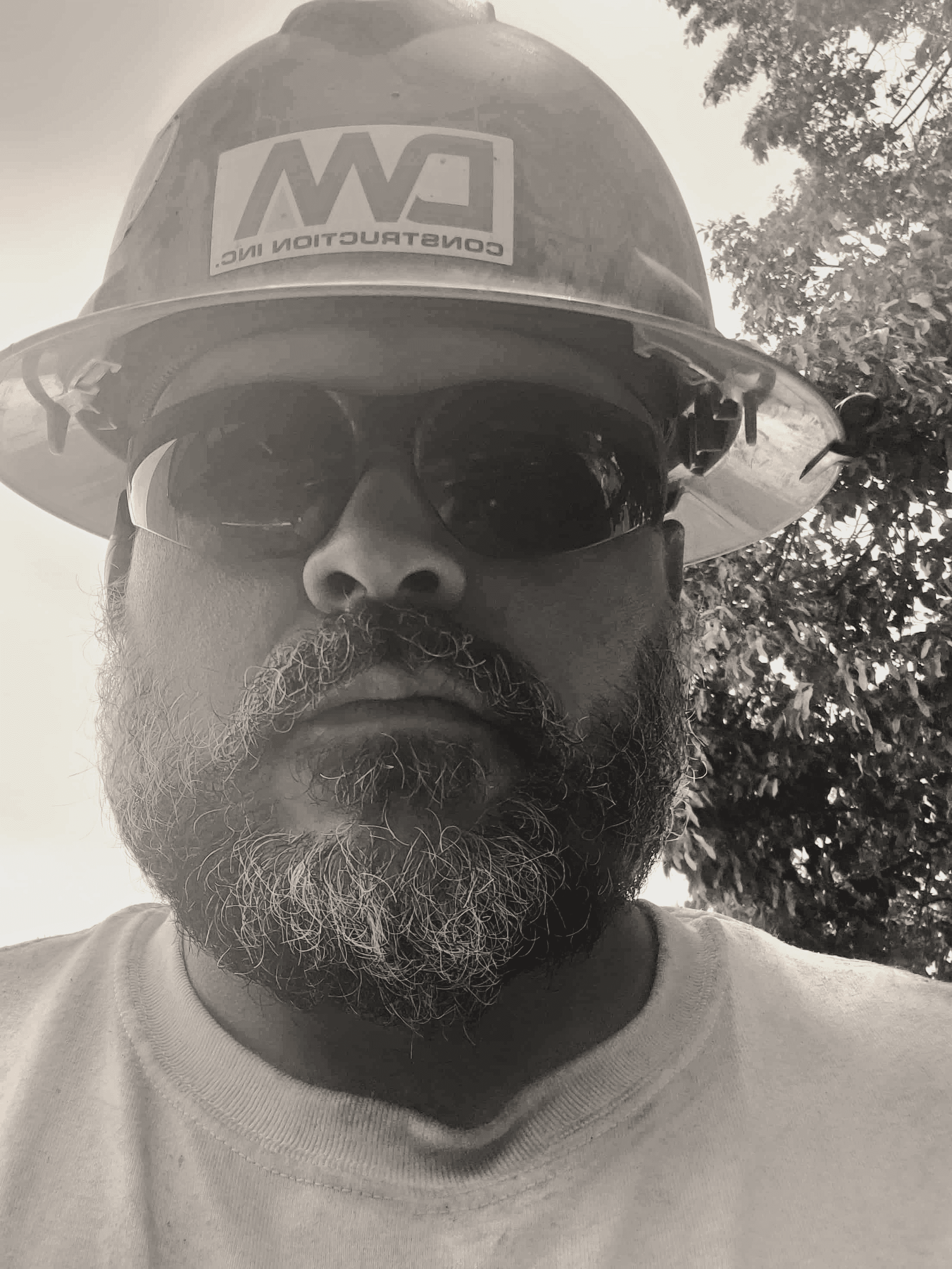 A man wearing a hard hat and sunglasses stares intently. His face has a beard. The hard hat has the logo "CW Construction". Chad Hintze Handyman.