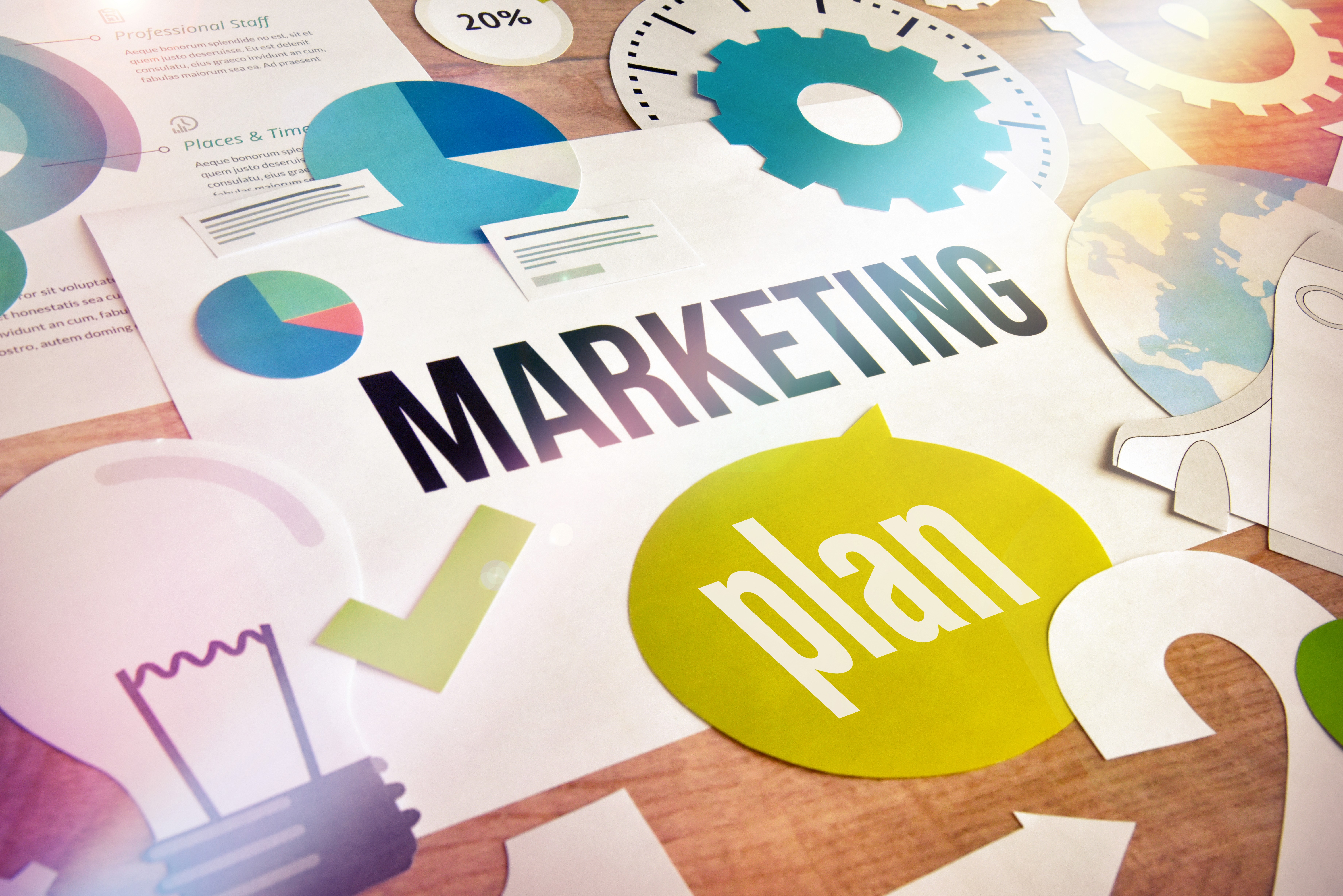 Colorful marketing plan documents, charts, and strategy materials spread across a table, representing the foundational infrastructure that gets built in the first month of a marketing system before results become visible