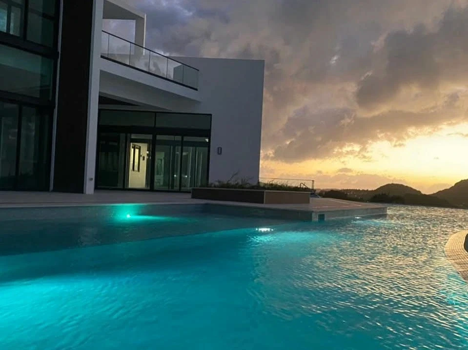 Infinity pool at The Hill Residence in St. Lucia, designed by Atelier International, glowing at sunset with hillside views beyond the edge.