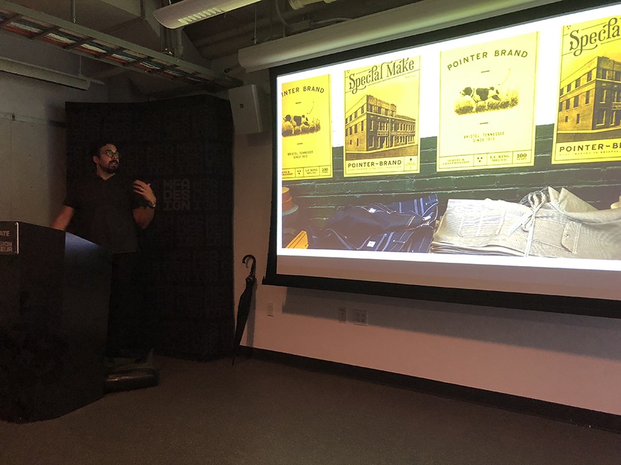 A photo of a man giving a lecture and looking at a projector screen where some yellow cards are depicted.