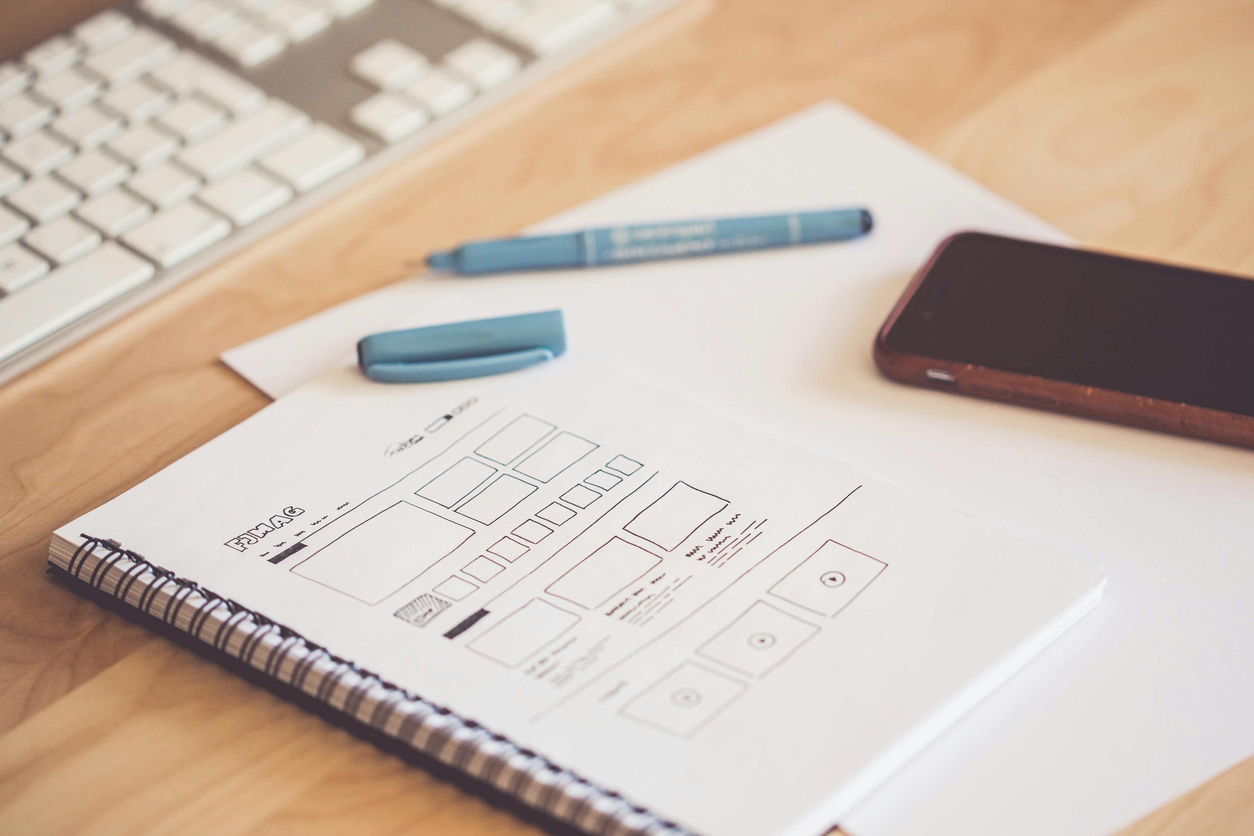 Product wireframes and interface sketches on a notebook beside a keyboard and smartphone