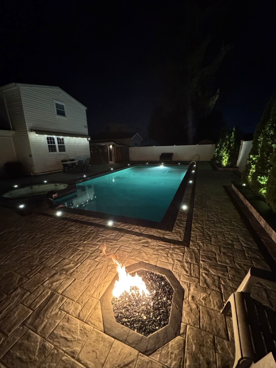 In-ground pool with fire feature at night by CMC Masonry on Long Island
