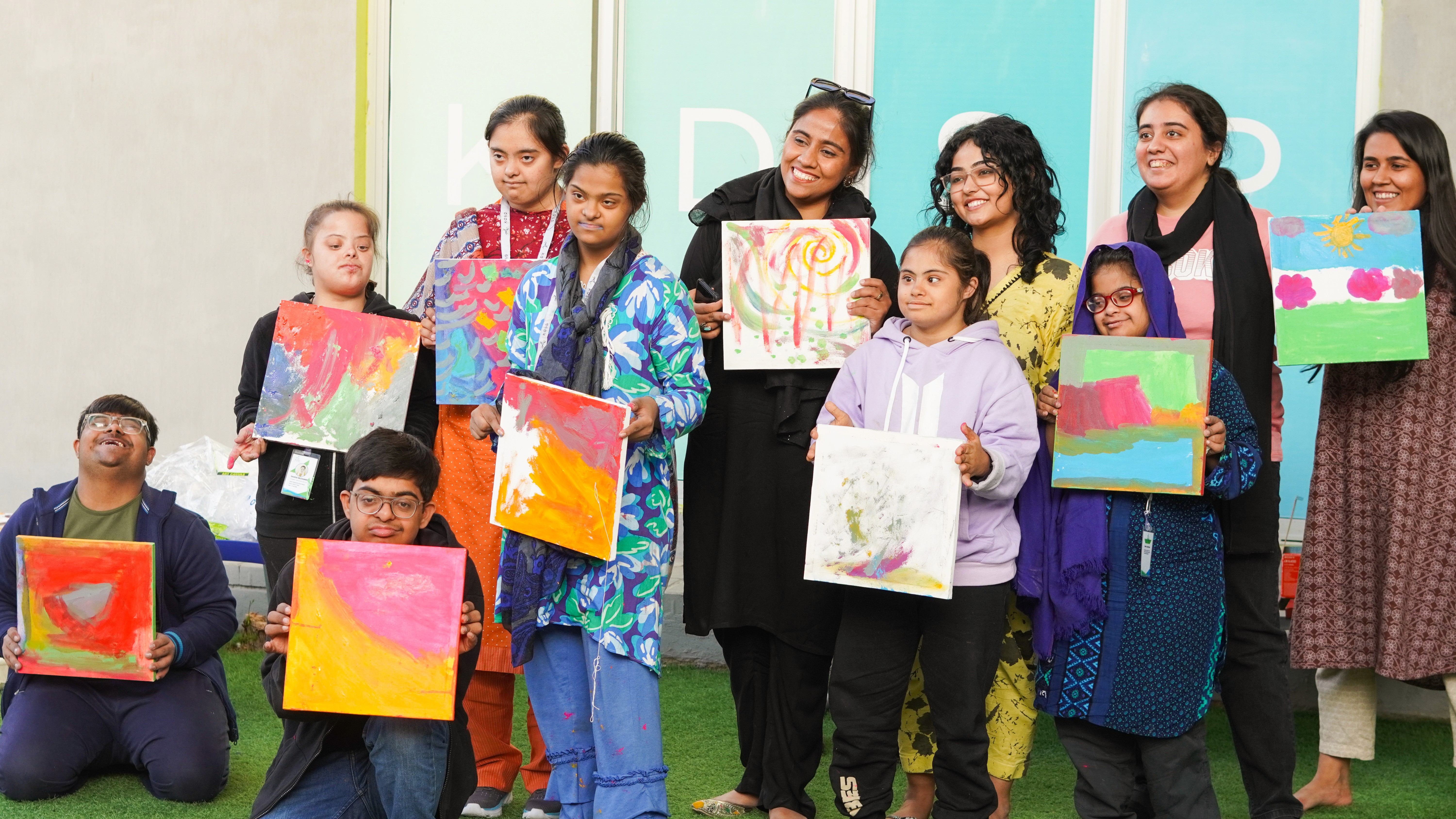 A group of children with down syndrome holding their artworks alongside two facilitators