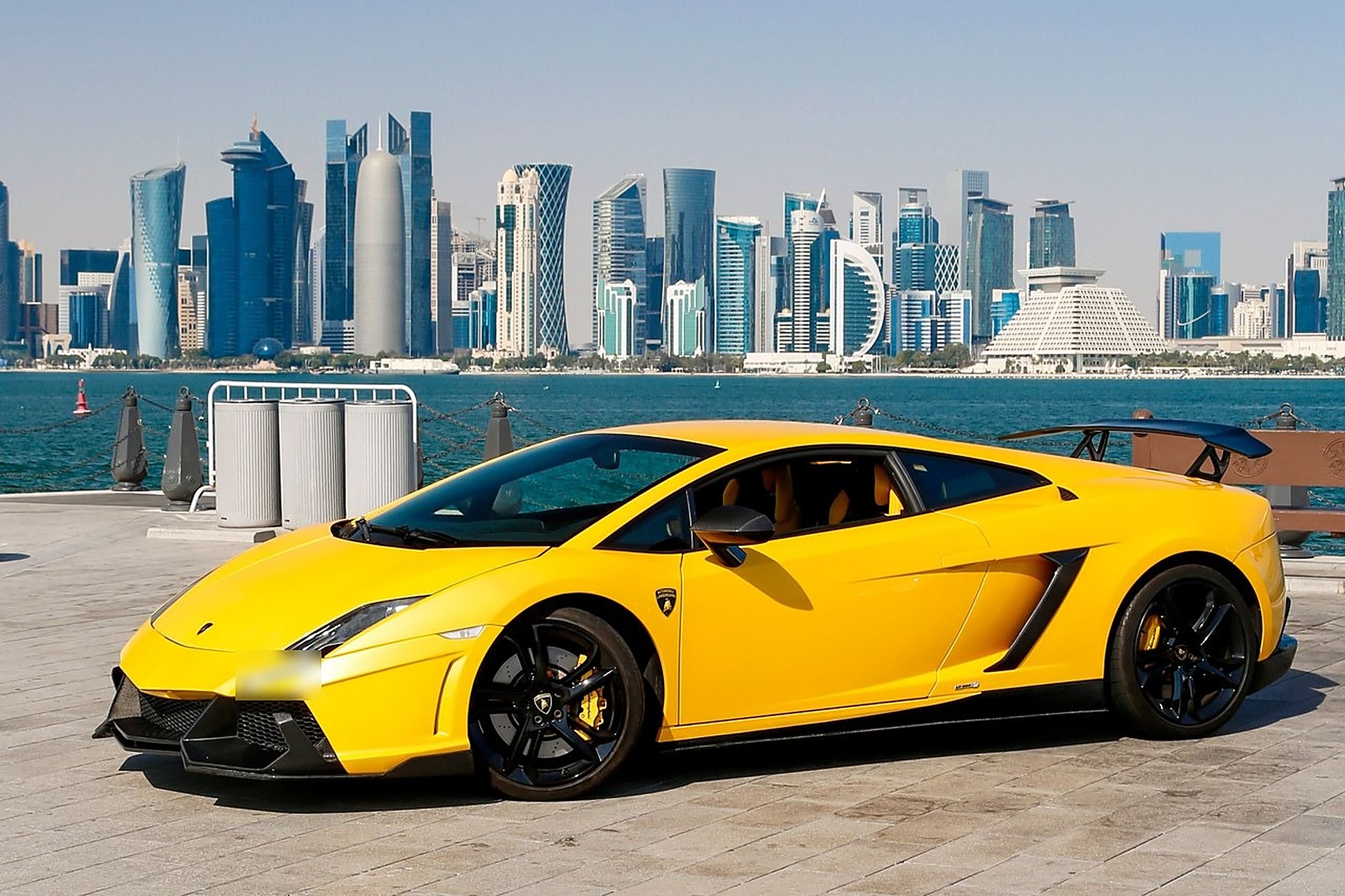 Une Lamborghini jaune garée au bord de l'eau, face aux tours de West Bay, à Doha, où une voiture coûte en moyenne 15 à 30 % de moins qu'en France