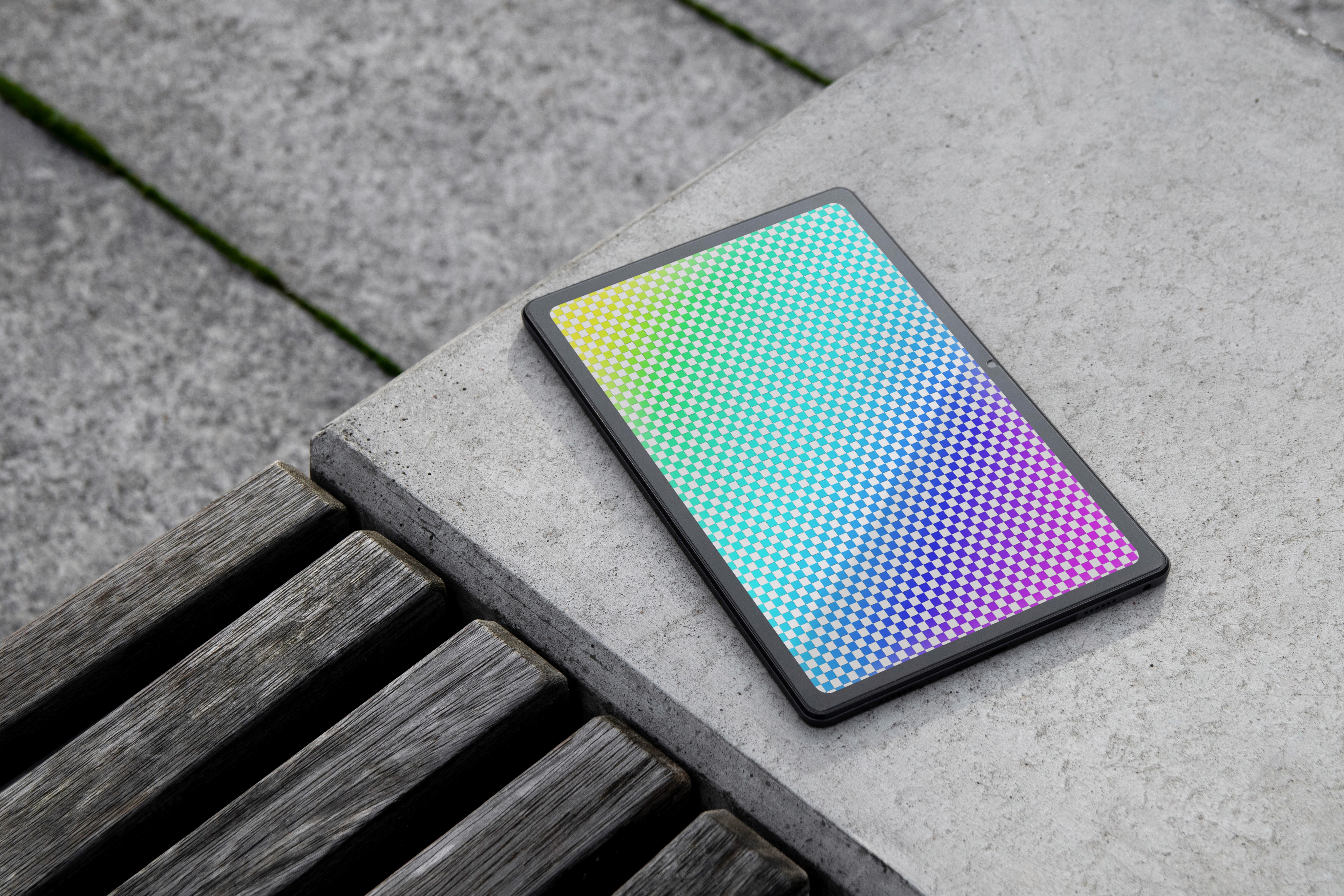 A tablet mockup featuring a colorful, iridescent geometric grid pattern on its screen, resting on a grey concrete ledge, used to represent dashboard usability and data hierarchy.