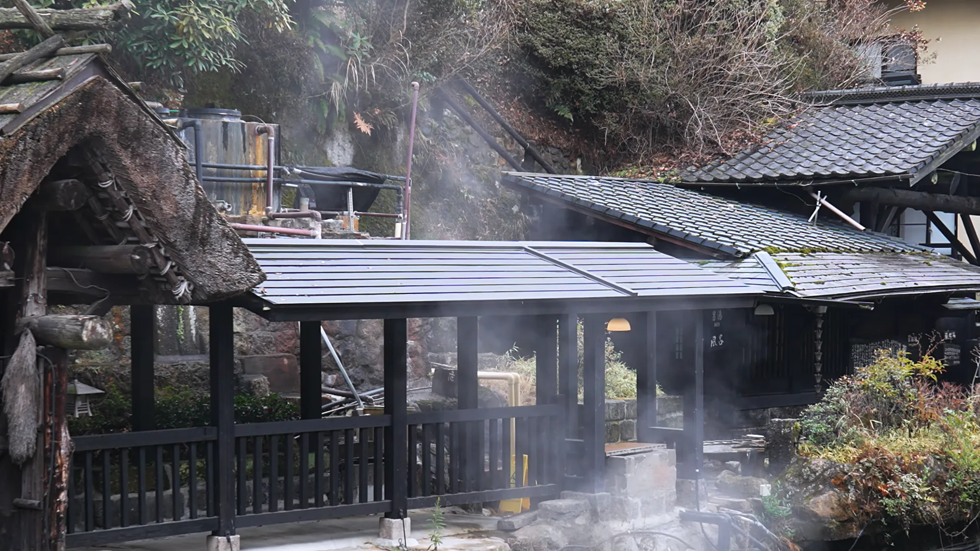 A steaming open-air bath at Kurokawa Onsen enclosed by timber buildings