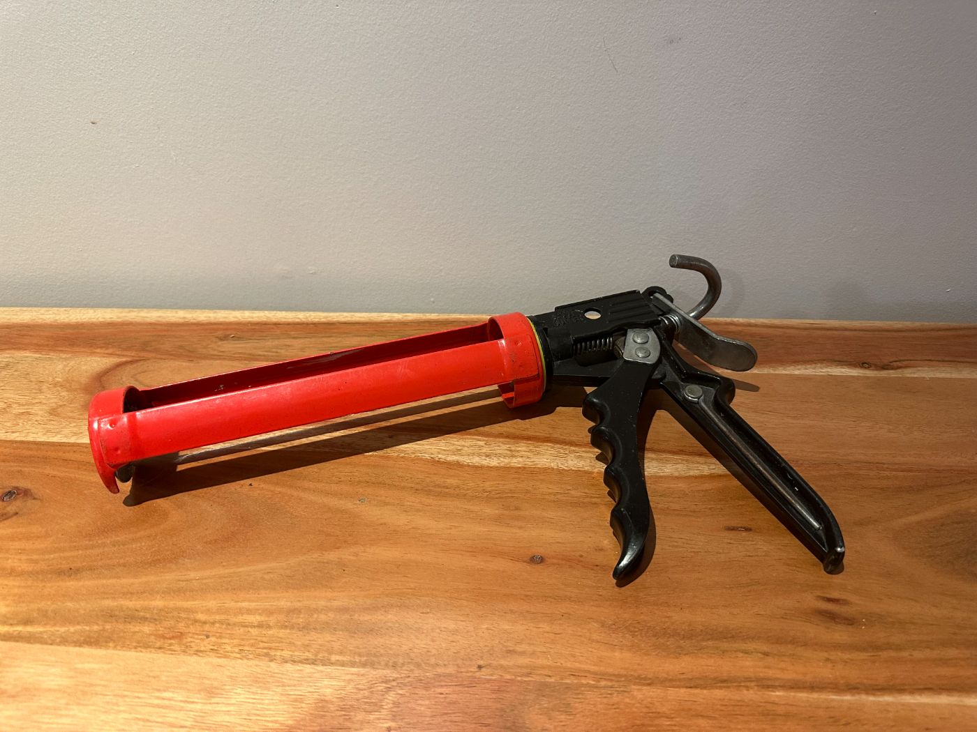 Pistolet à calfeutrer rouge et noir posé sur une table en bois