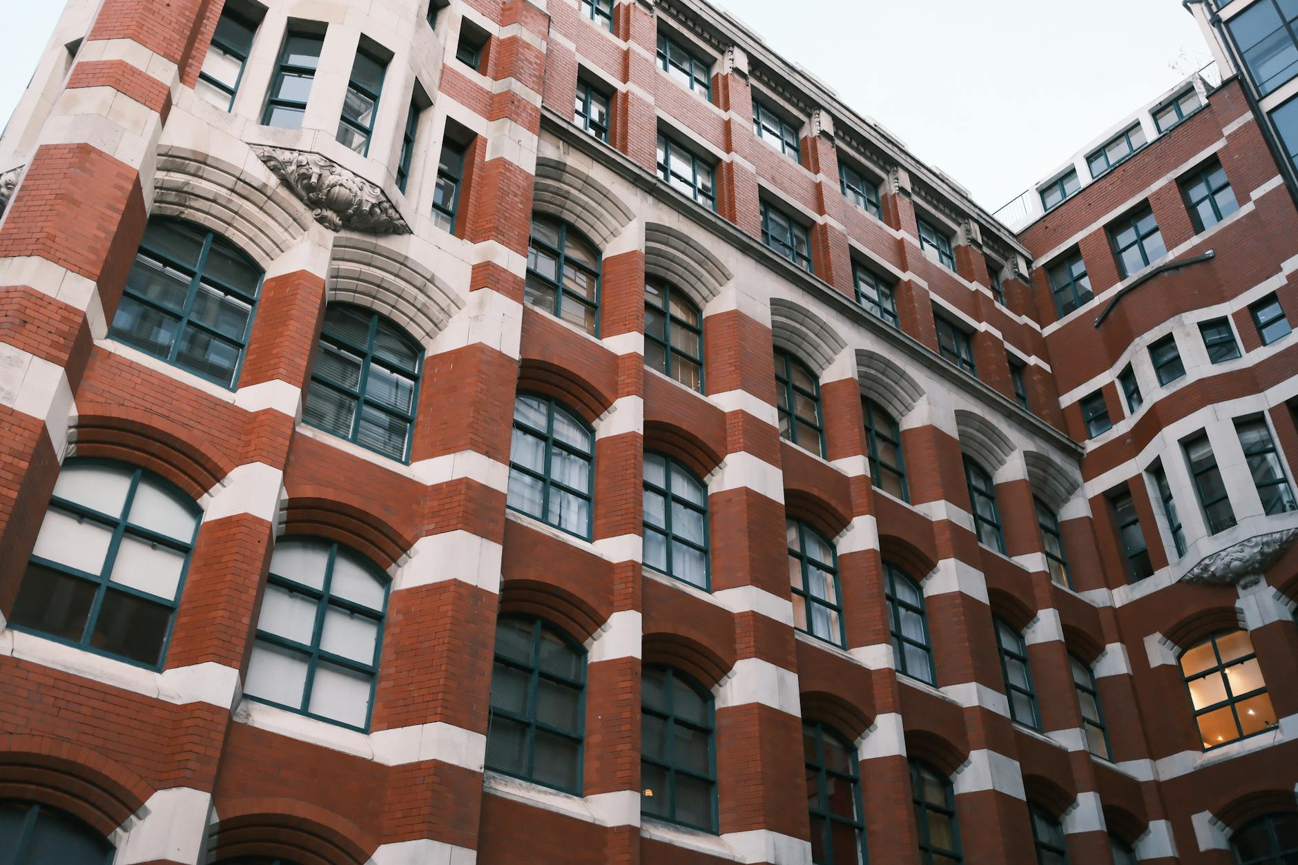 Ornate Victorian red brick building with white stone-trimmed arched windows viewed from a low angle against a grey sky