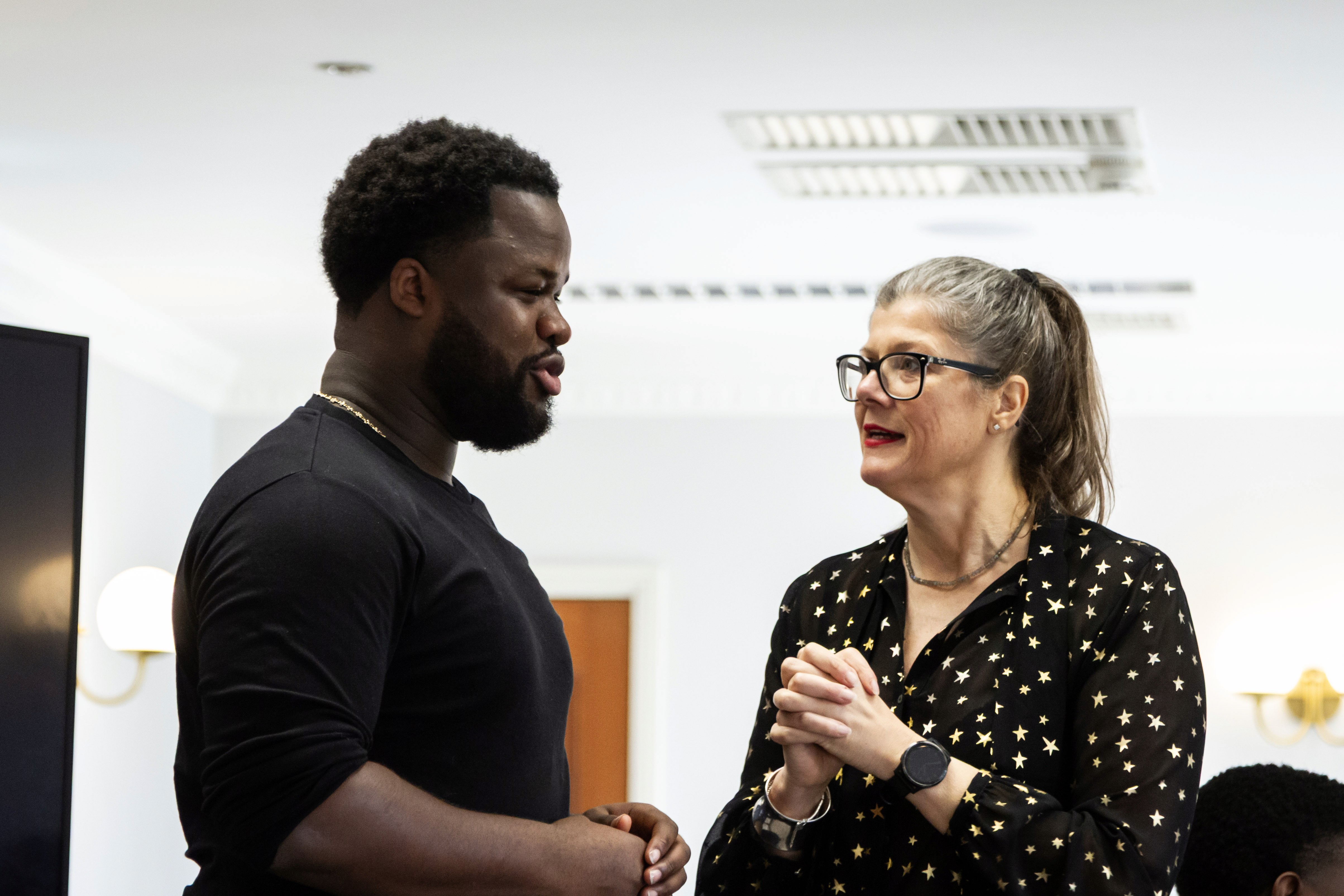 Man in black shirt talks to woman with glasses and polka dot shirt.