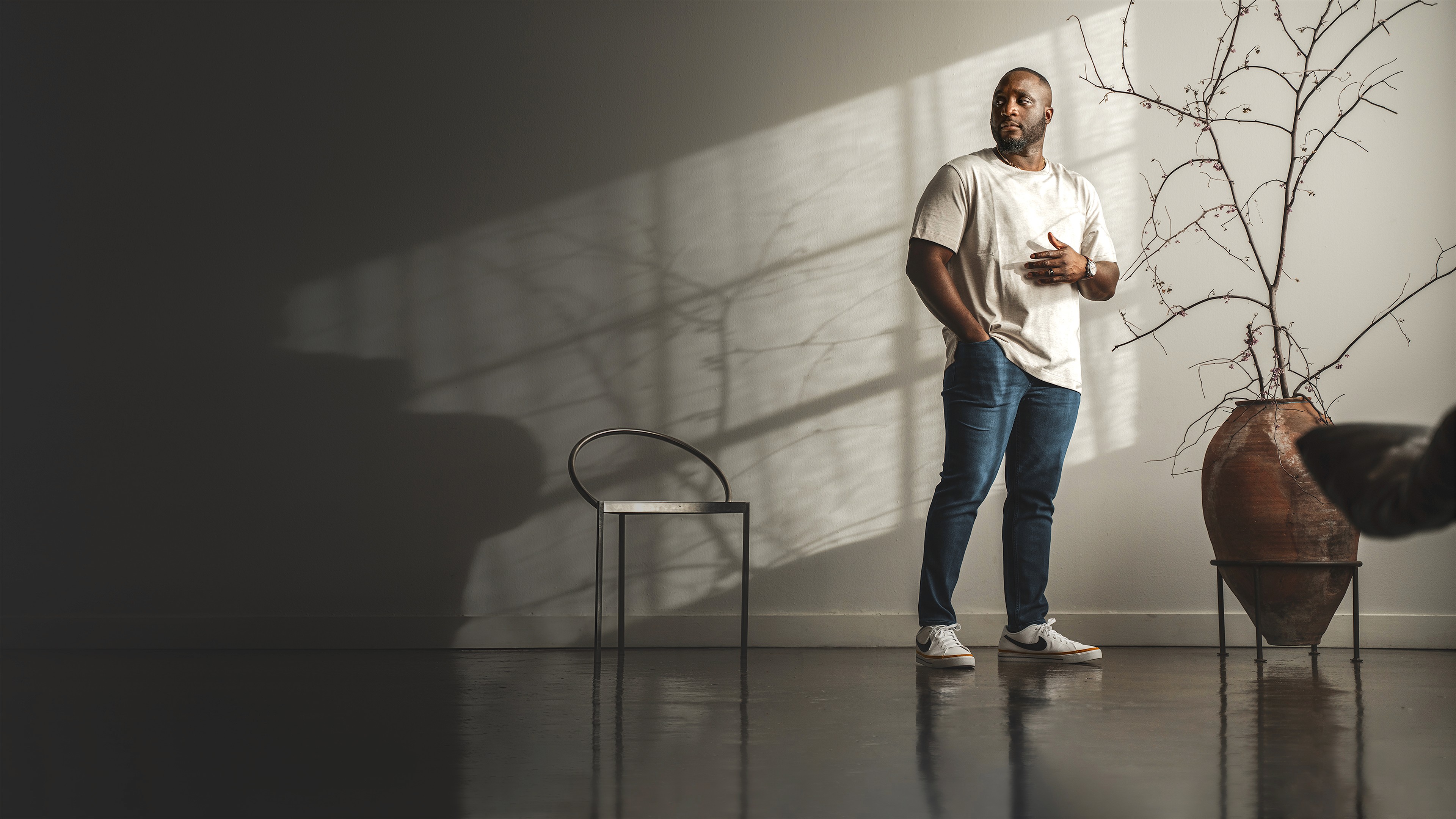 Tade Bolarin, executive and life coach for ambitious professionals, standing in a Japandi minimalist loft, wearing casual beige t-shirt, blue jeans, and Nike shoes.