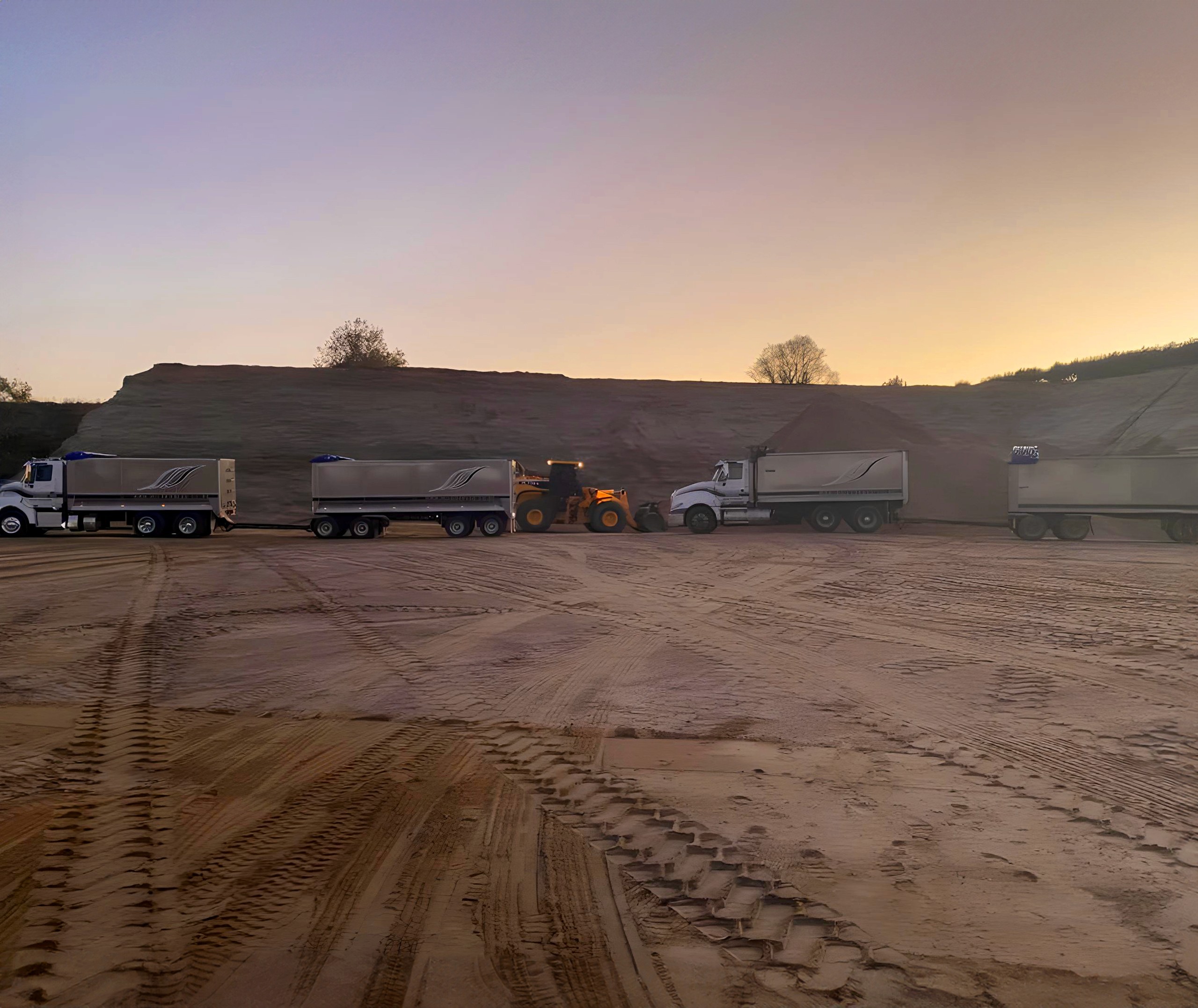 Two trucks and a loader in a sand quary at dawn