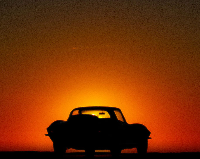 A red sports car parked in-front of a sunset.