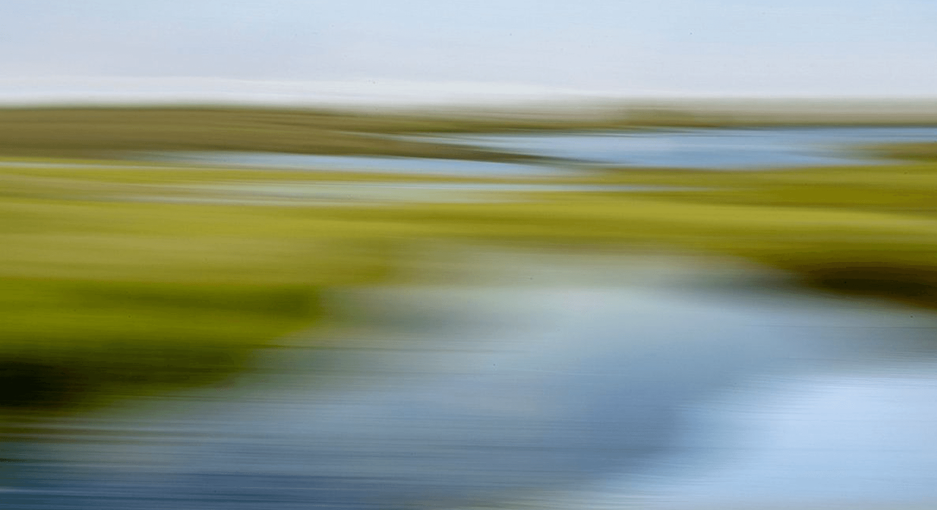 Woman smiling while seated at a desk with a laptop as a man in glasses leans over to show her something on the screen.