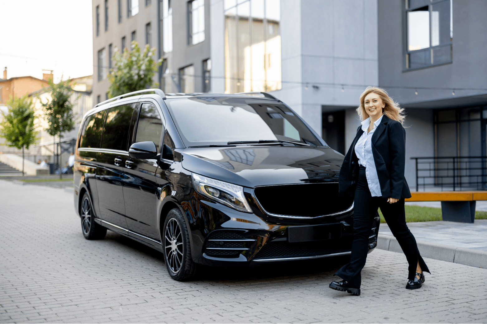 Woman in business attire standing beside a luxurious black chauffeur van in an urban setting, promoting States Car Service's commitment to elegant and reliable transportation.