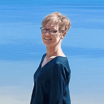 Heilpraktikerin Iris Löcher steht vor einem blauen Meer und lächelt freundlich in die Kamera