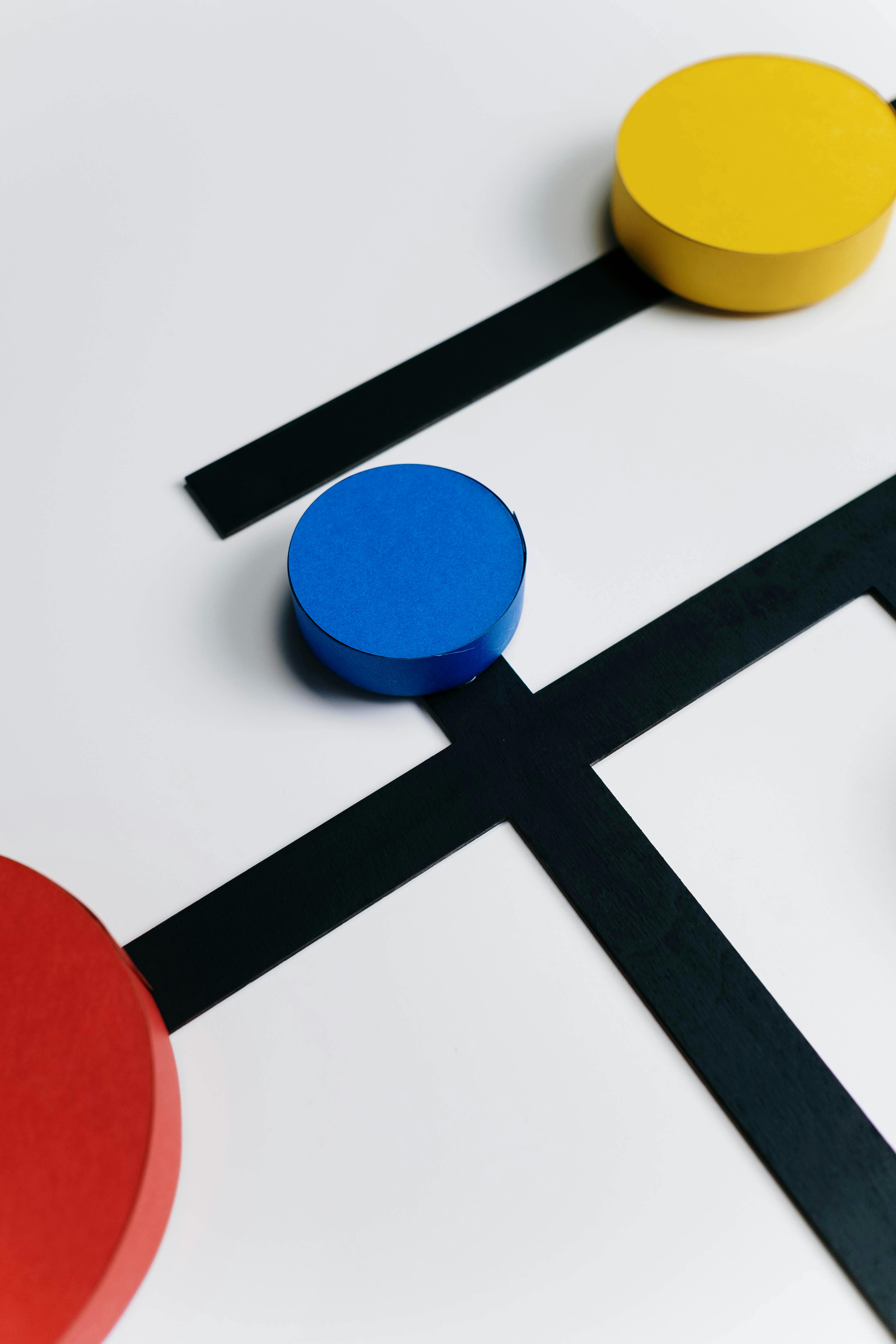 A minimalist abstract design featuring red, blue, and yellow circles connected by intersecting black lines on a white background.