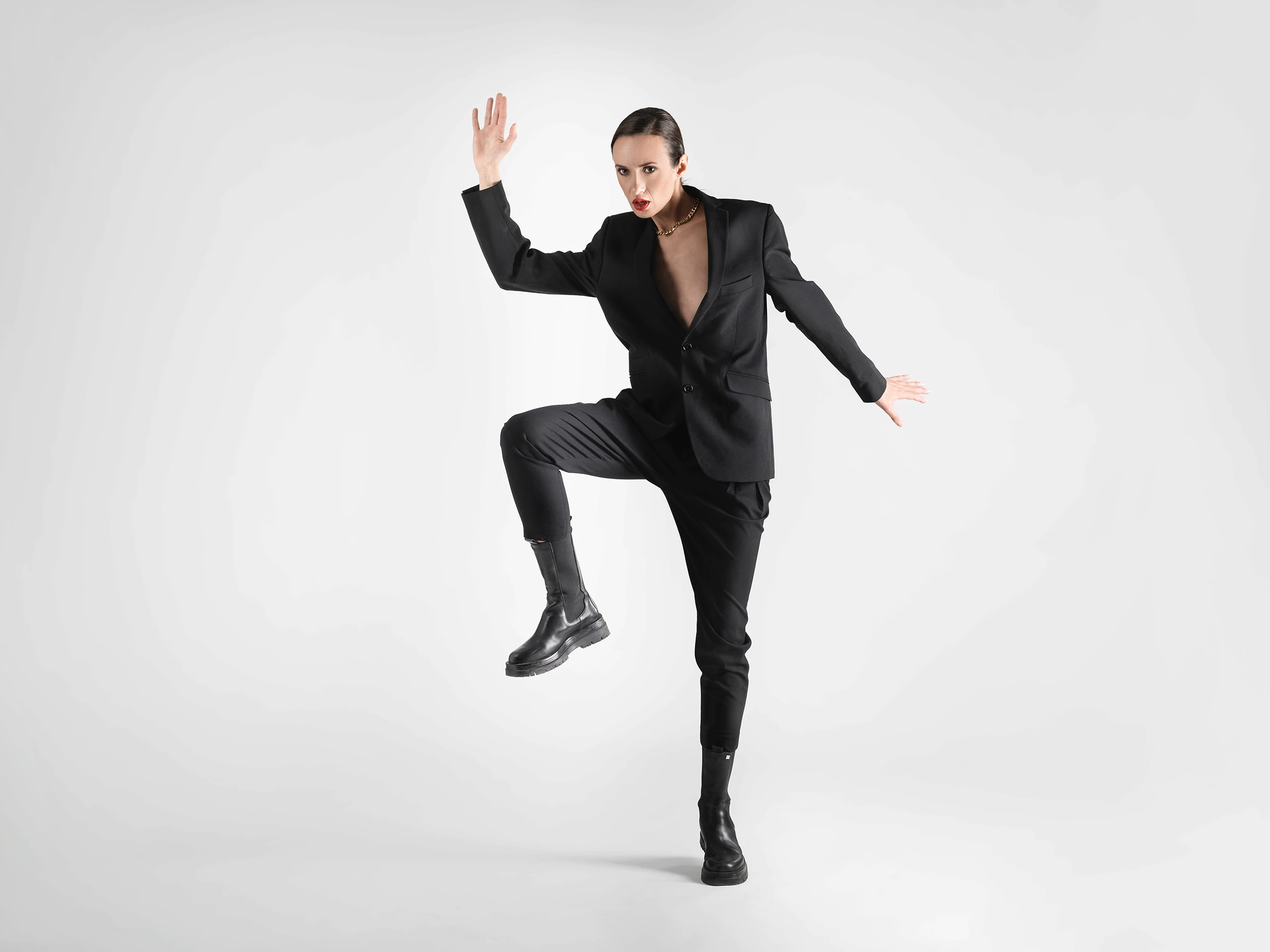 Strong fashion pose of a woman in a black suit, captured in motion against a clean background.