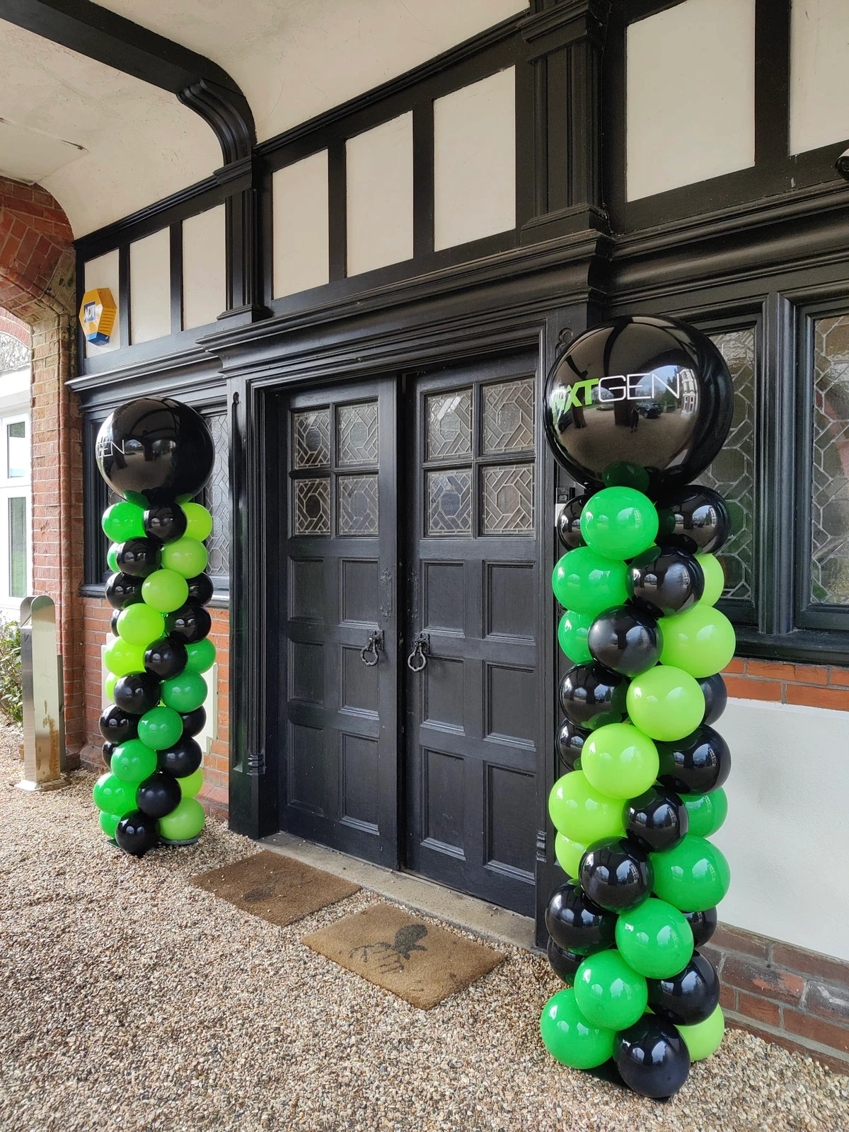 Black and green spiral balloon columns placed outside a dark-wood front door