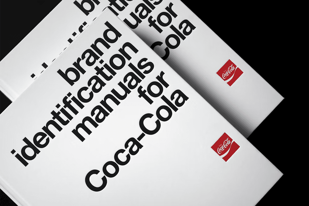 Coca-Cola brand identity manuals stacked together, showing how brand guidelines document logo, typography, and visual system usage.