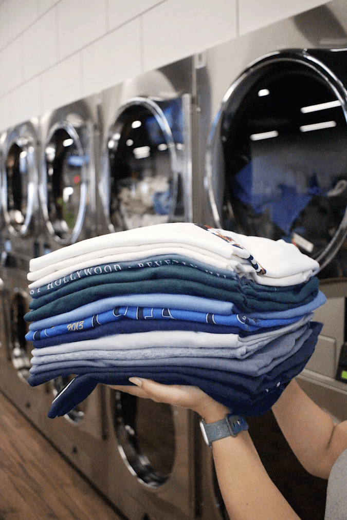 Folded laundry ready for delivery in front of commercial dryers at a Brooklyn laundromat – part of Soap and the City’s pickup and delivery service.