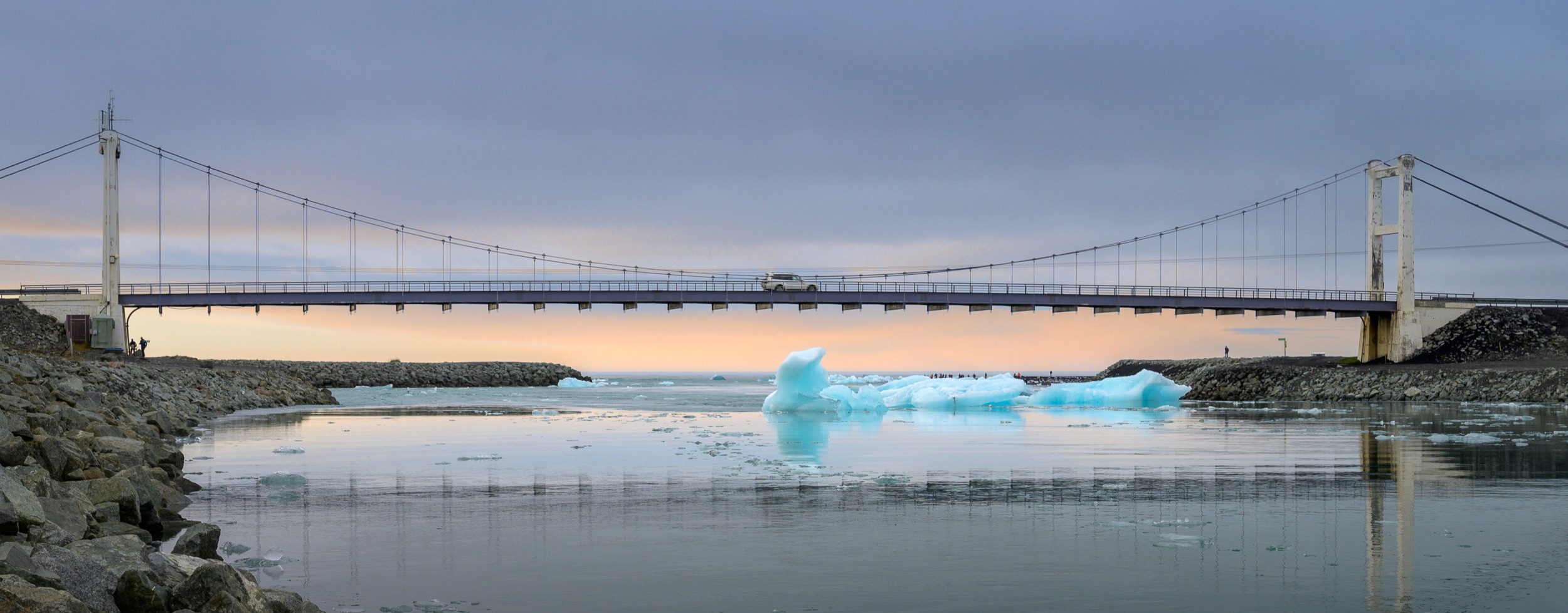 Glacier Lagoon bridge with a car driving on it and an iceberg in the foreground in Iceland