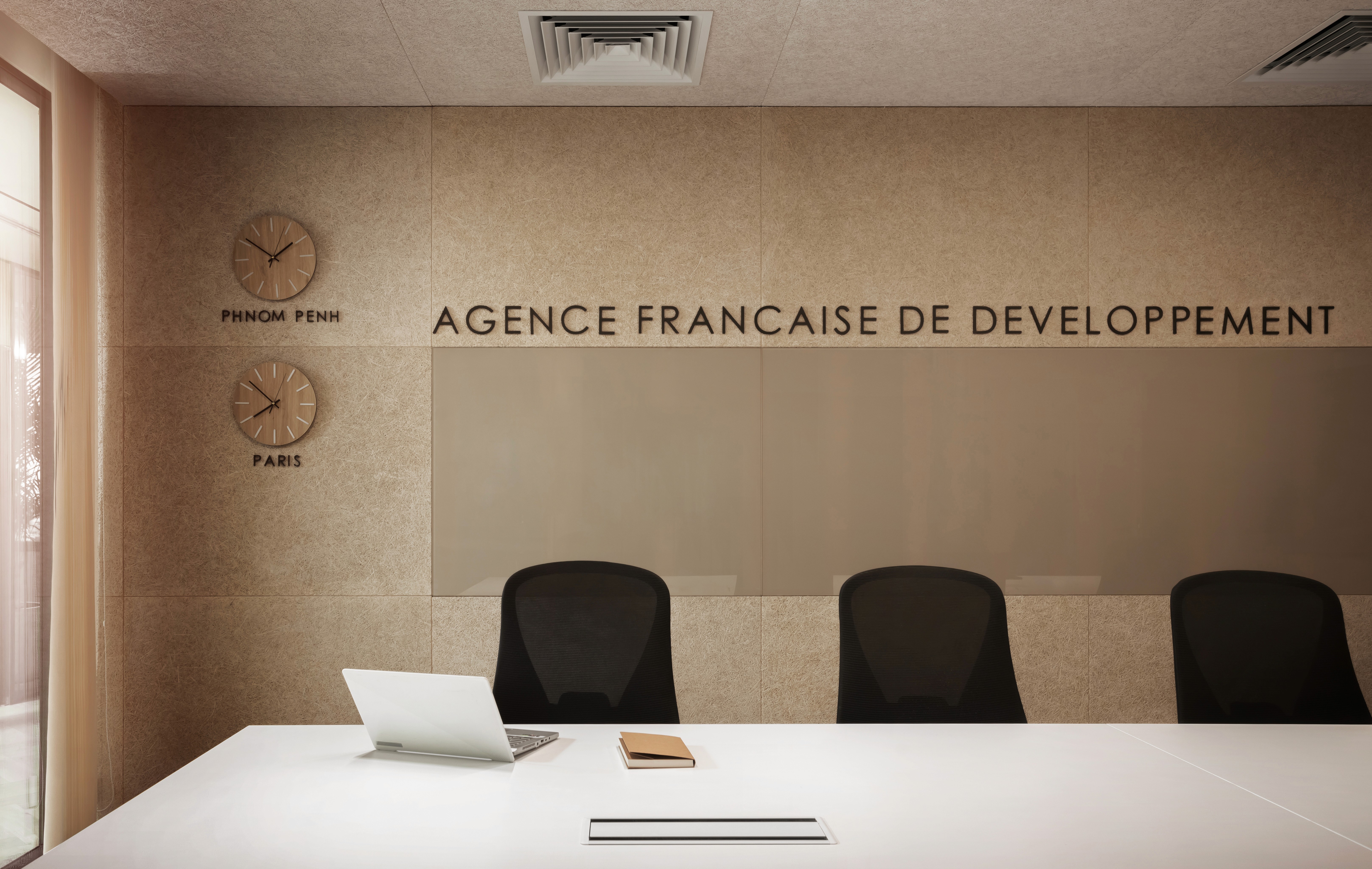 Meeting room with brand wall signage, dual time zone clocks, and neutral material palette reinforcing corporate identity