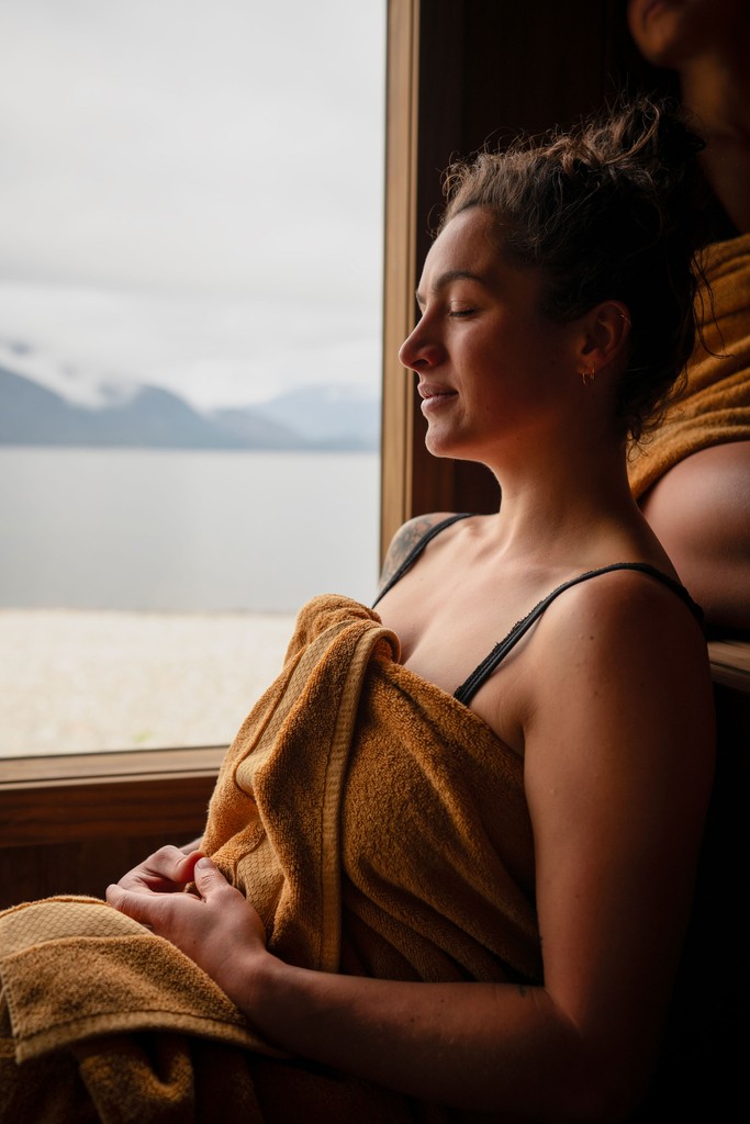 Woman sitting in sauna by herself with a towel wrapped around herself