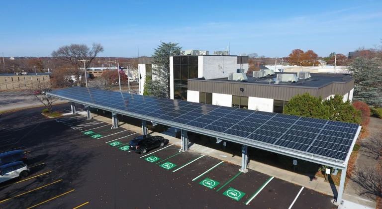 Aerial view of a building with a solar panel roof, surrounded by parking spaces and clear blue sky.