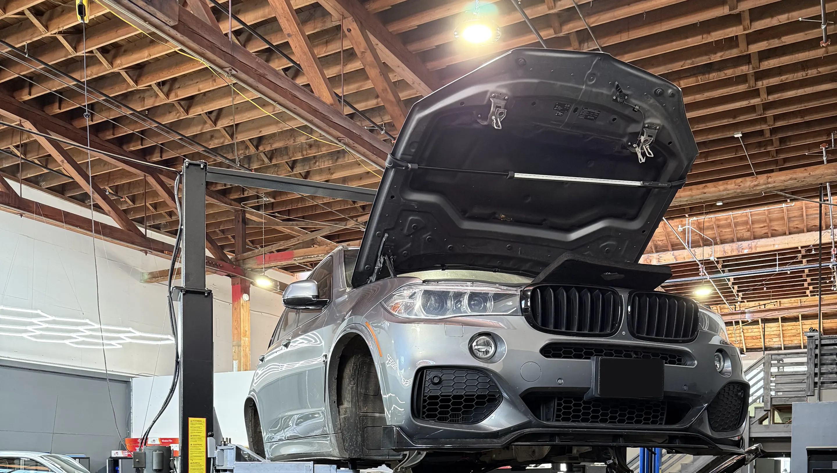 Silver BMW SUV raised on a lift with its hood open in the workshop