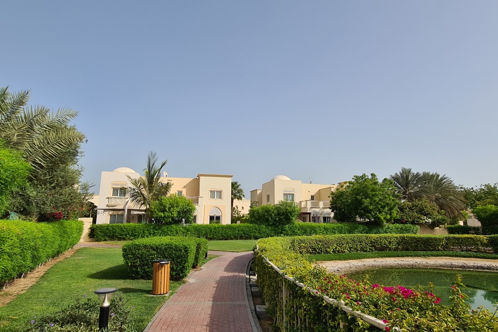Walkway leading to a tranquil garden with a pond and trees in the Springs 2 community.