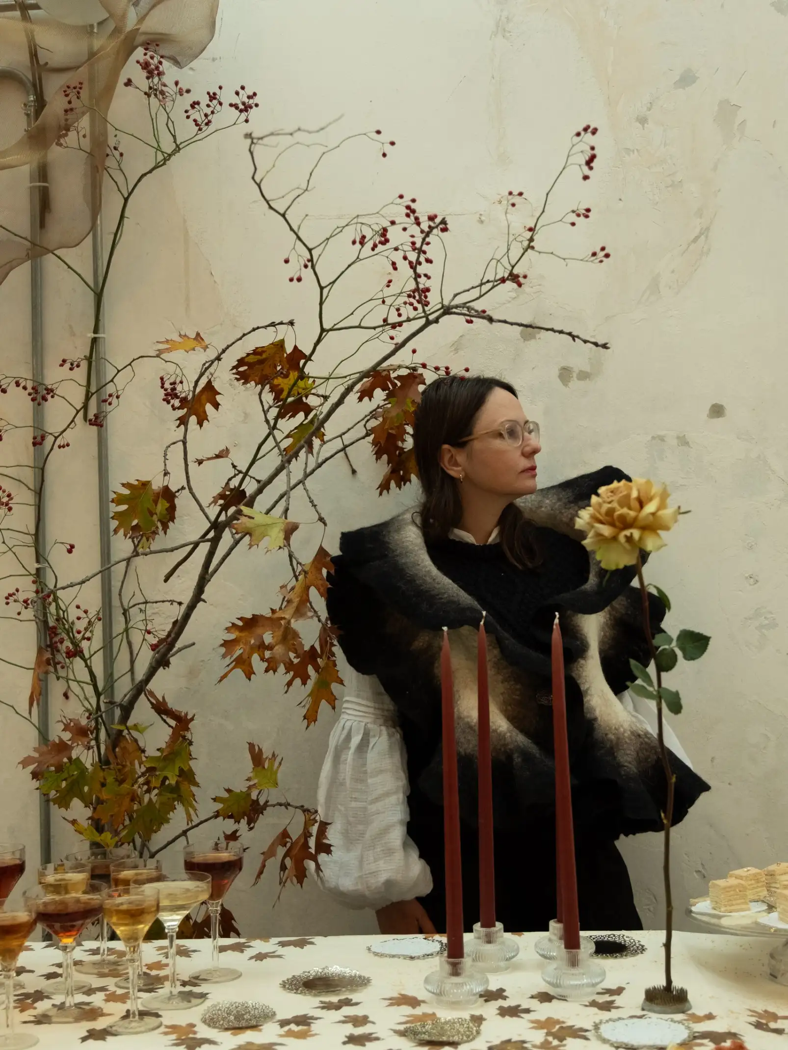 Retrato de Irina Khatsernova en entorno floral con velas y copas para instalación sensorial, representando elegancia natural.