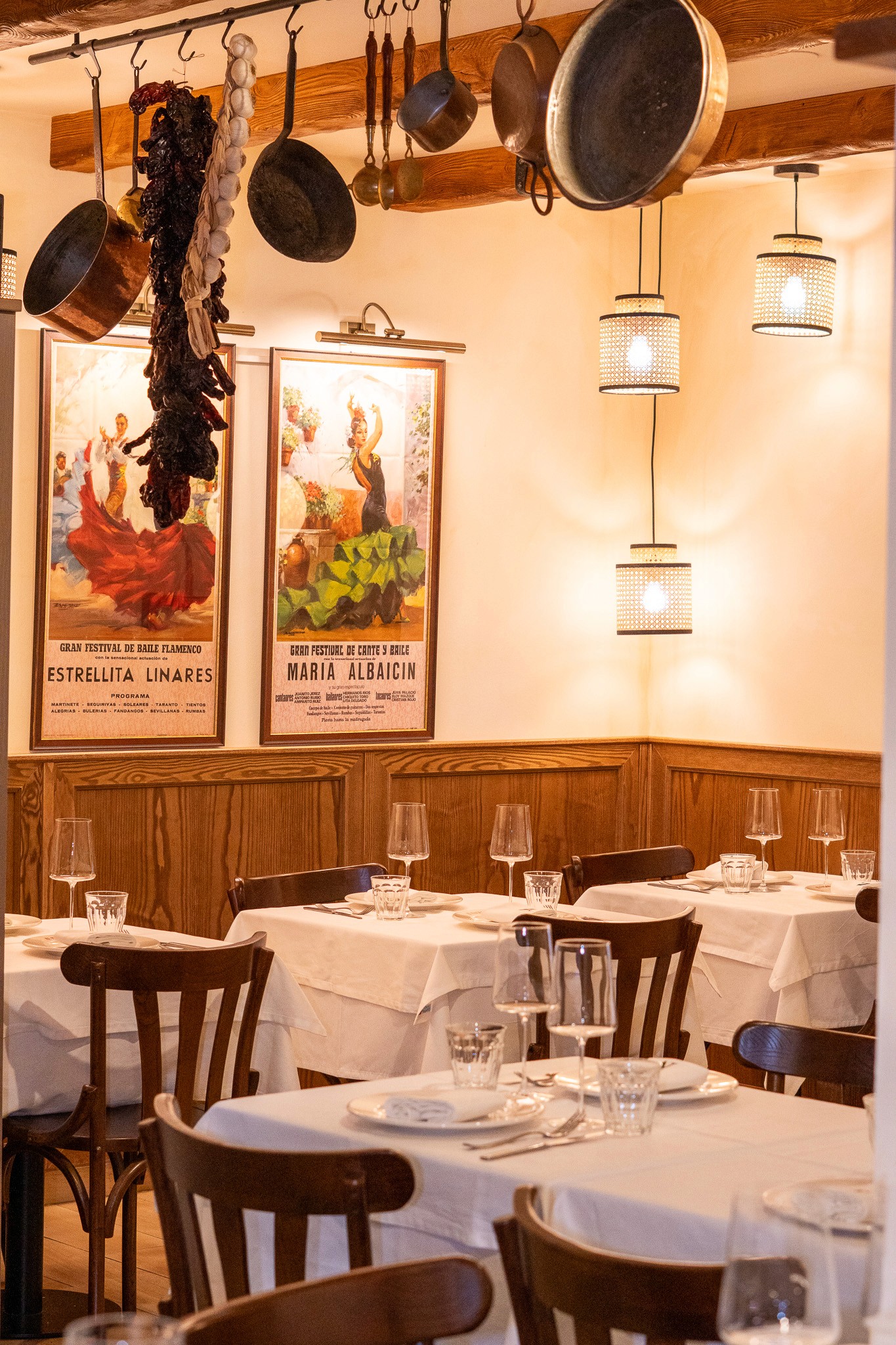 White plate with roasted carrots served on green sauce, topped with almonds and fresh herbs, held by a hand over a dark table.